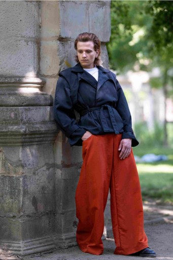 Profile portrait of a woman wearing sculptural red-and-gold earrings against a deep burgundy background