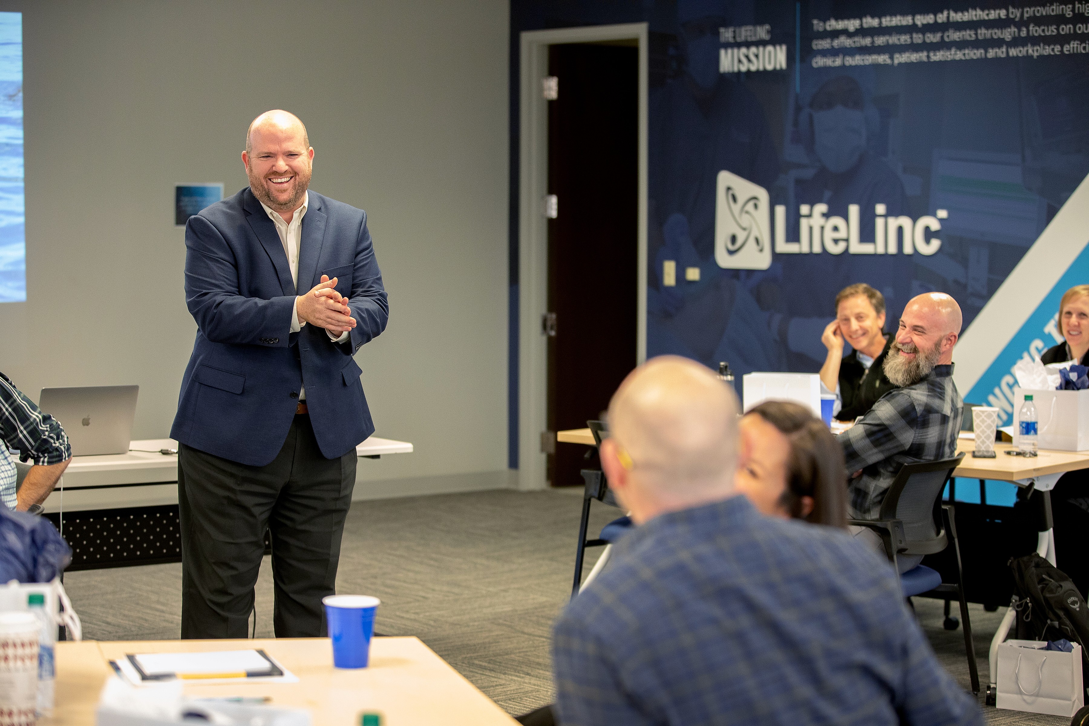 A LifeLinc LEAP program facilitator smiles and engages with attendees during a Leadership Empowered Anesthesia Providers clinical leadership training retreat, with the LifeLinc branded banner visible in the background."