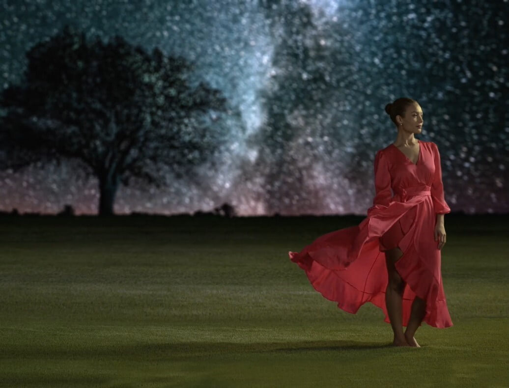 A pretty woman wearing a red dress walking on luxurious AGL artificial grass under the stars.