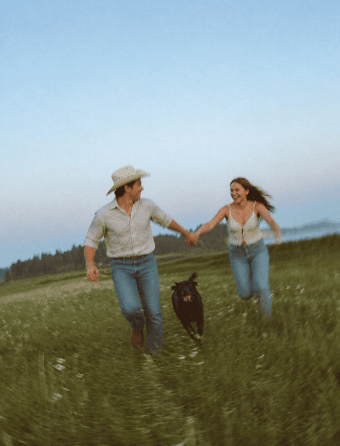 Couple running through a meadow at dusk with their dog