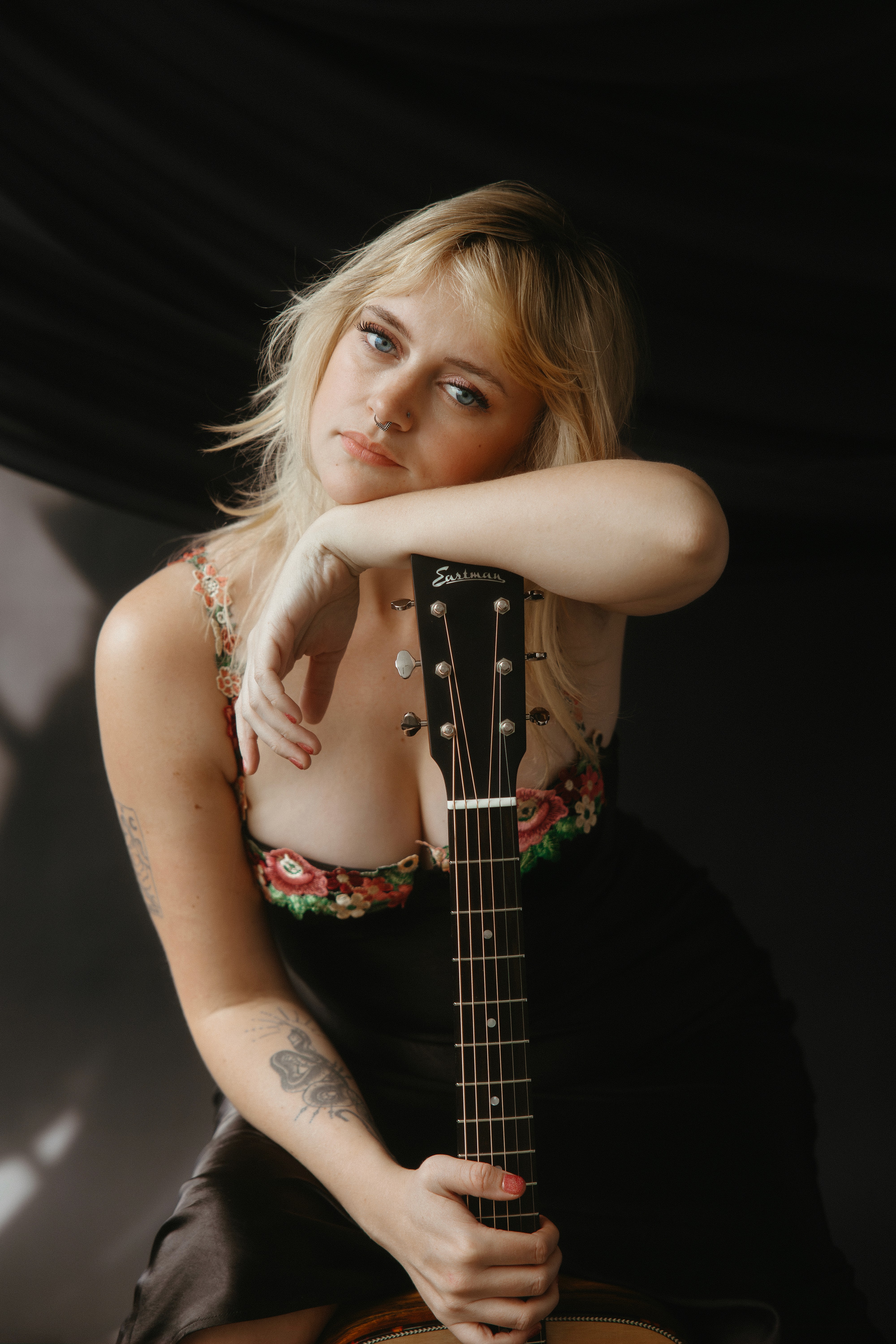 Country music artist poses resting her head on her guitar, looking right into the lens