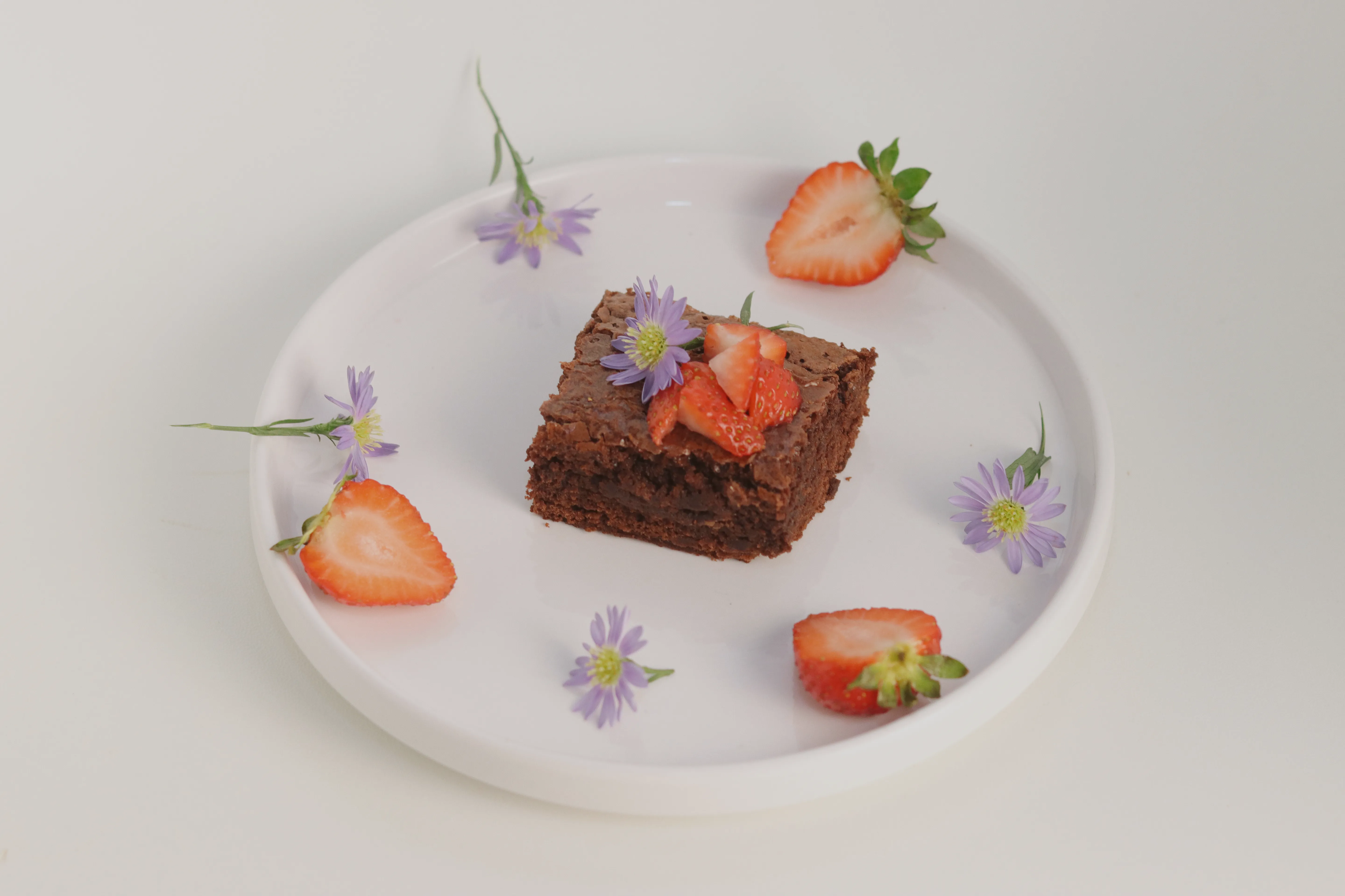 Brownie con fresas y flores lilas sobre fondo blanco