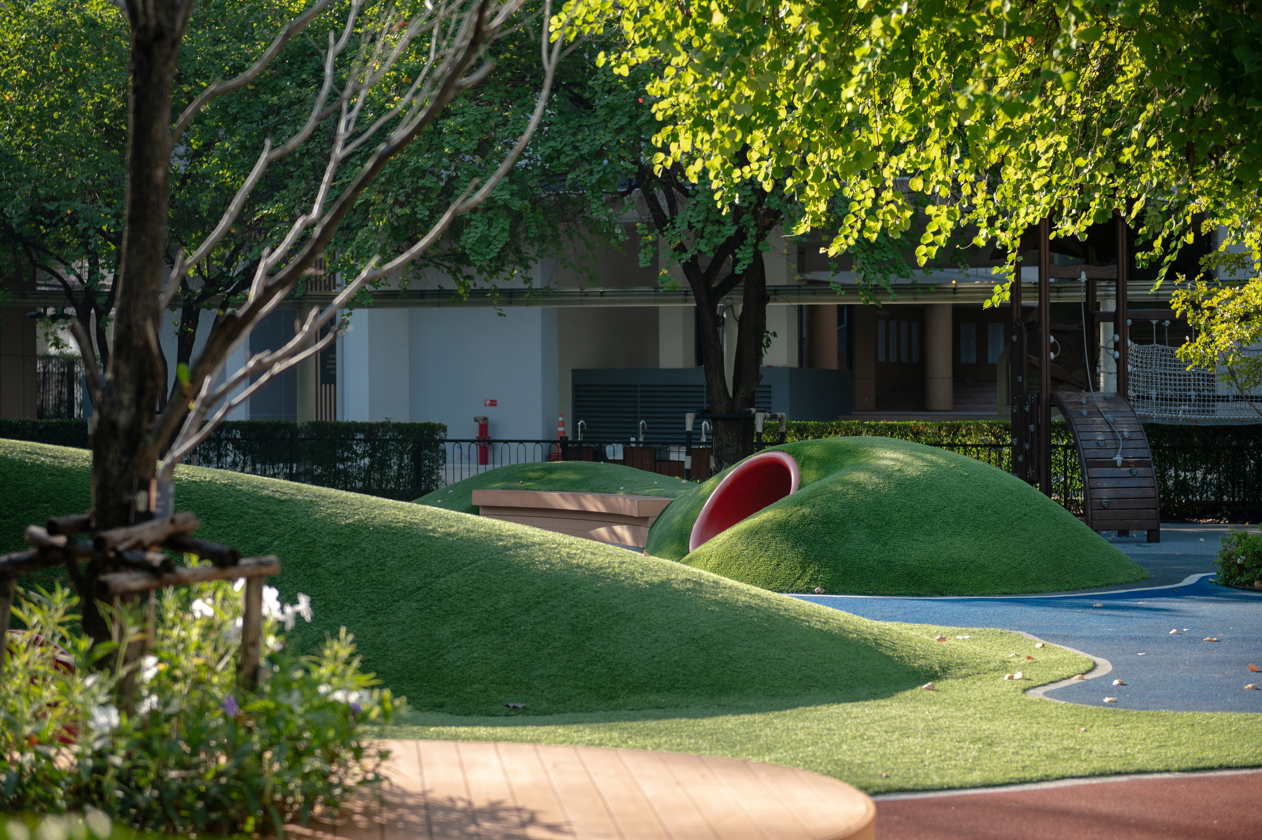 Nature-inspired children’s play landscape featuring soft artificial grass mounds, a tunnel slide, and shaded outdoor play elements integrated into a modern residential courtyard.
