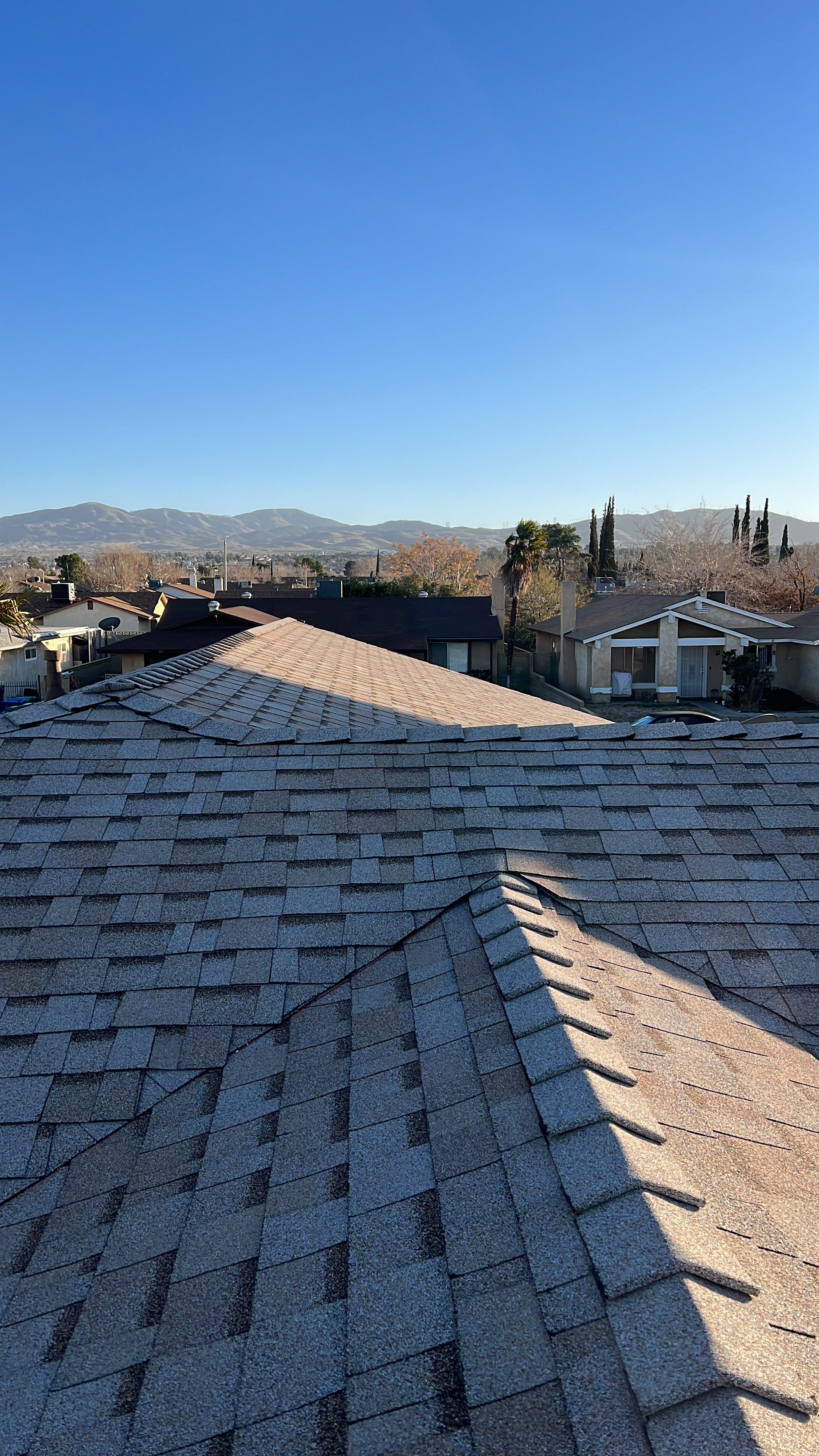 A modern house with large windows and a flat roof, surrounded by greenery against a clear blue sky.