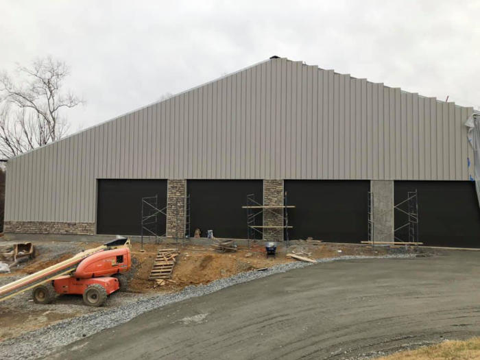 A large, gray building under construction with black doors, surrounded by dirt and construction materials.