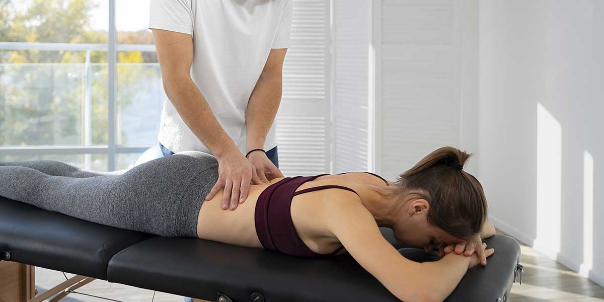 A therapist applies targeted lower back pressure to a woman on a table, demonstrating massage therapy for sciatica pain.