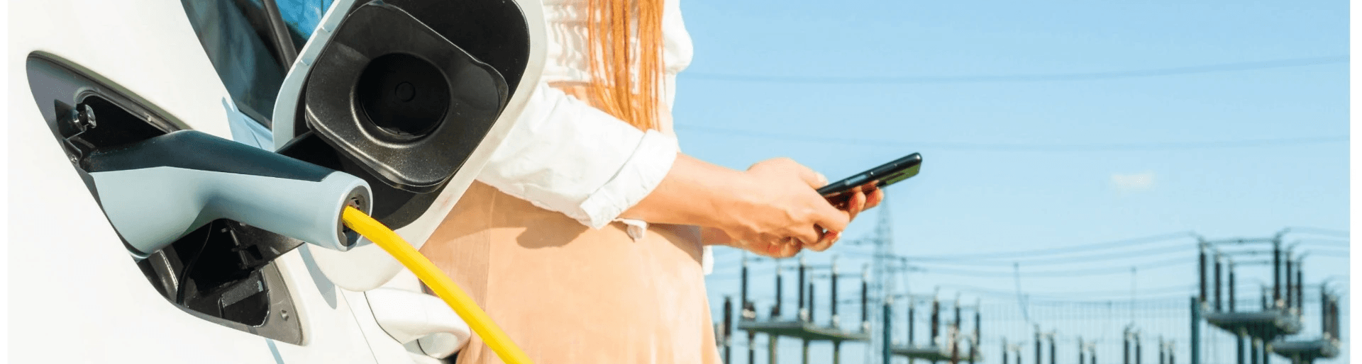 Person charging an electric vehicle while using a smartphone, symbolizing the integration of digital technology with electric mobility and the convenience of managing charging processes in Switzerland