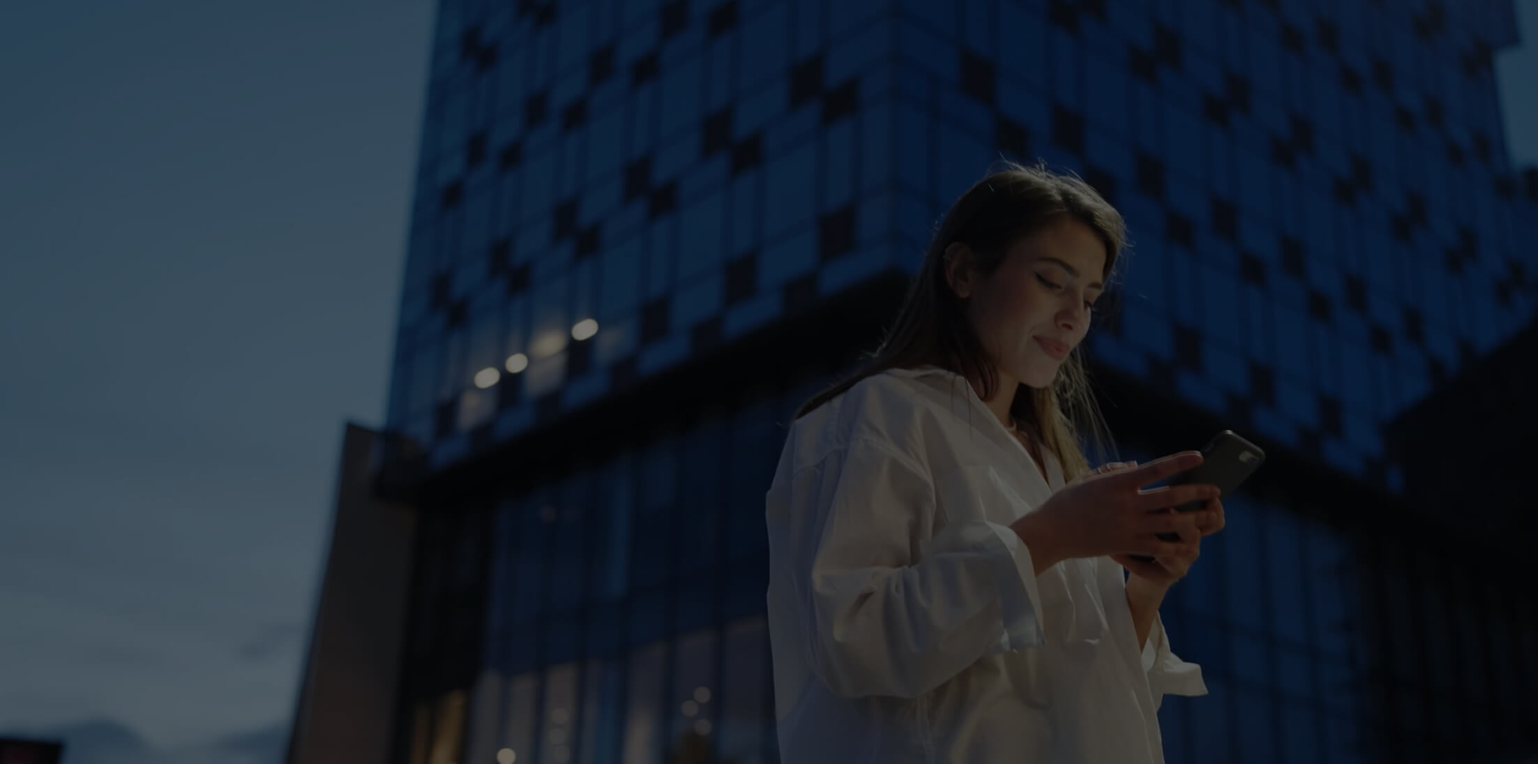 Woman standing outside an office building holding her phone and looking at it