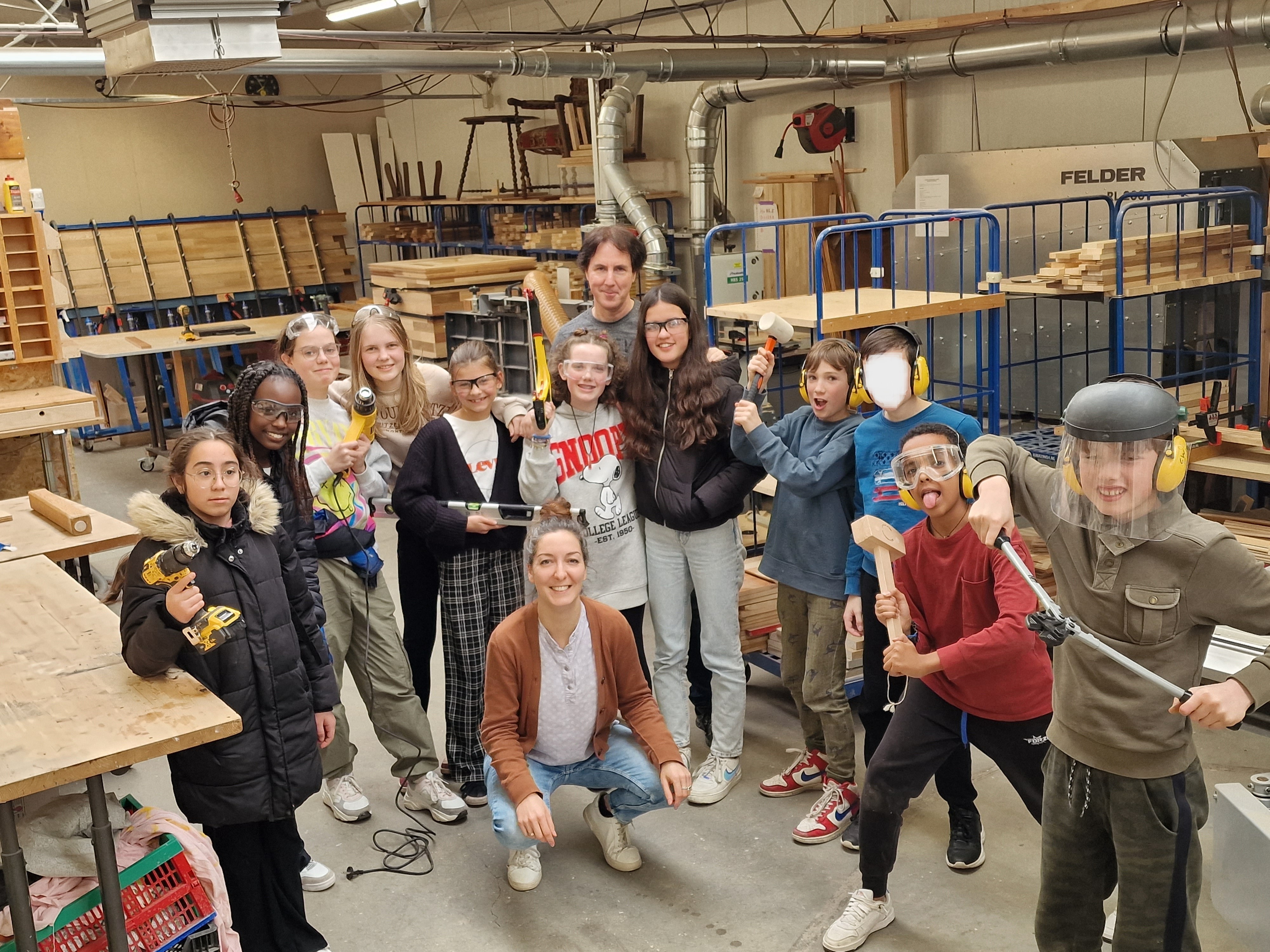 Groep kinderen en twee volwassenen poseren met gereedschap in een houtwerkplaats