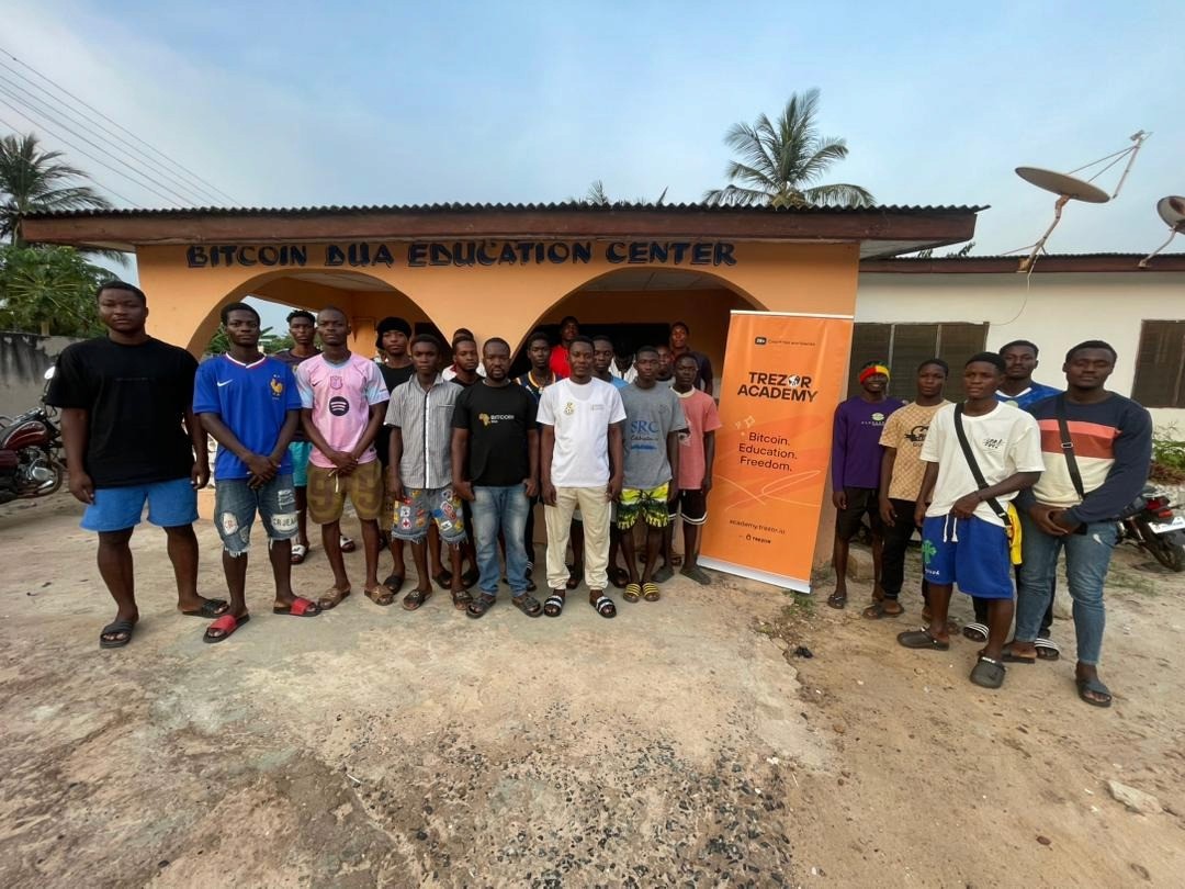 Bitcoin Dua founder Kofi Folivi in a black Bitcoin Dua T-shirt standing with community members outside the Bitcoin Dua Education Center in Agbozume, Ghana