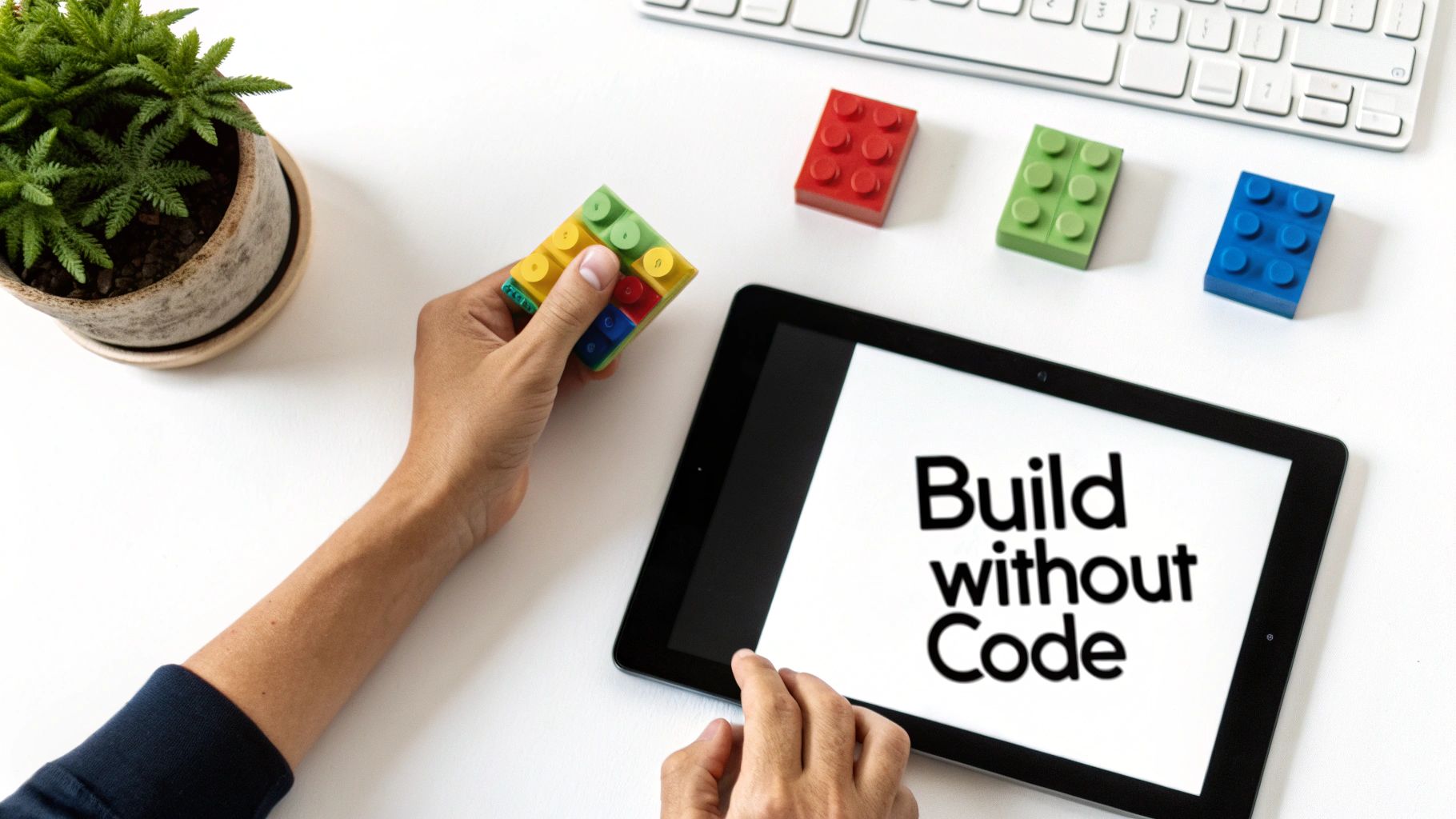 Overhead view of hands arranging colorful building blocks next to a tablet displaying 'Build without Code'.
