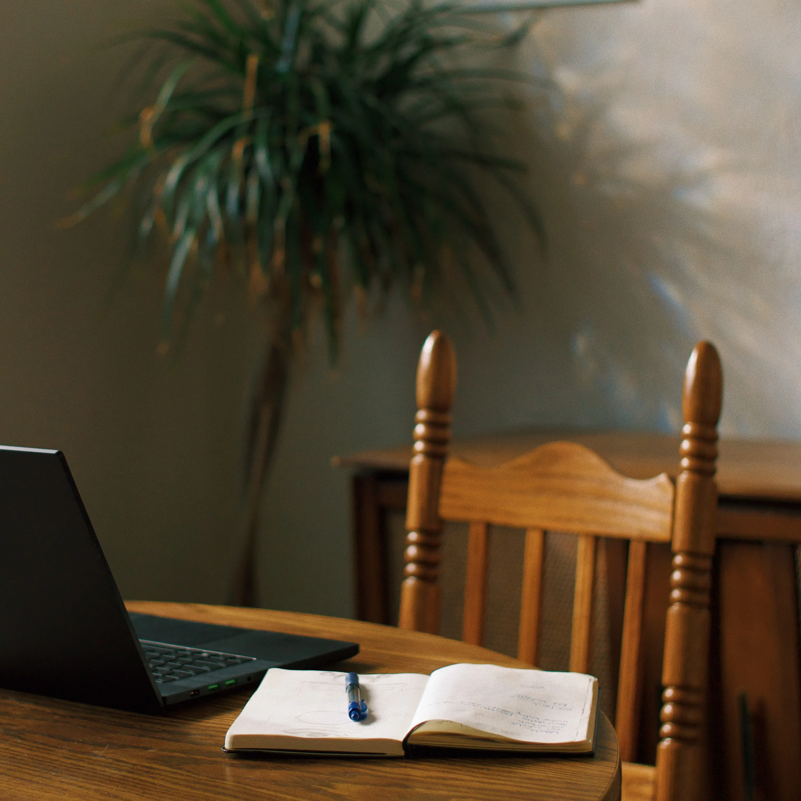 Home workspace with a laptop, open notebook, and pen on a wooden table