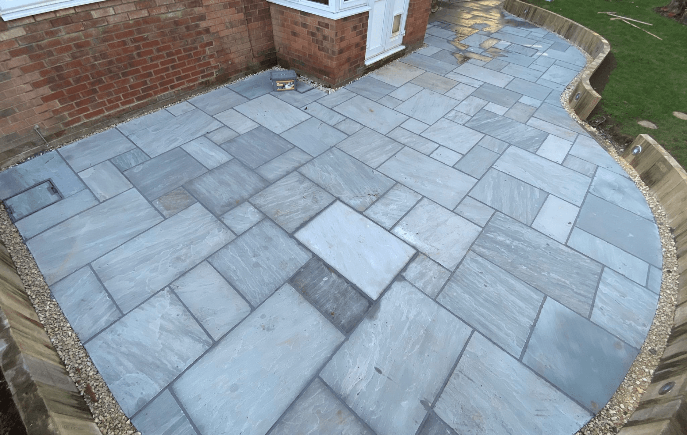 Newly installed Indian sandstone patio by PPM Builders in Northampton, featuring a curved design with a wooden sleeper border. Expert patio installation for a stylish and durable outdoor space.