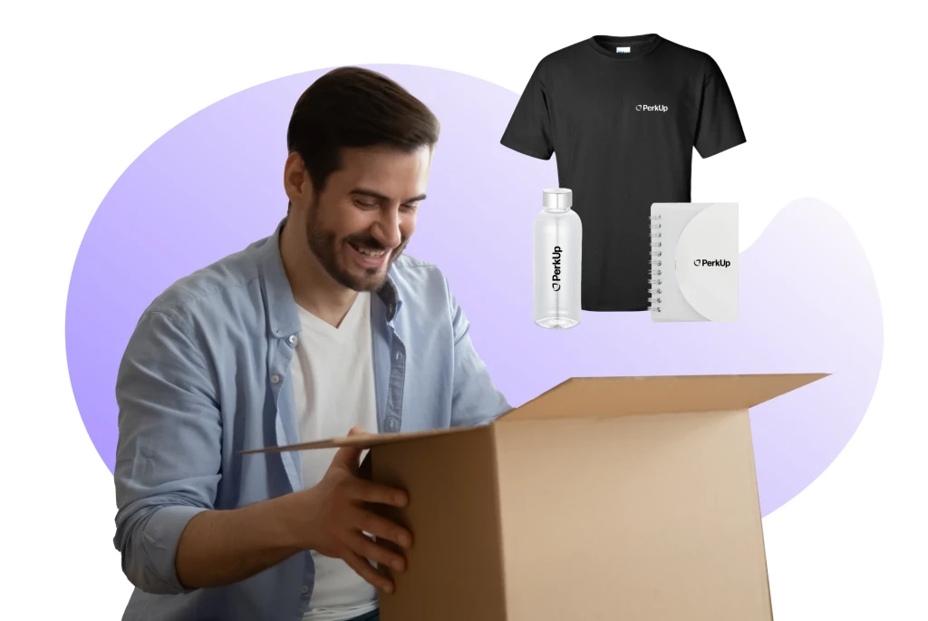 Man excitedly opening a box of branded company swag including a company T-shirt, water bottle, and notebook. Ideal for boosting employee morale and promoting brand visibility through affordable, high-quality swag items.