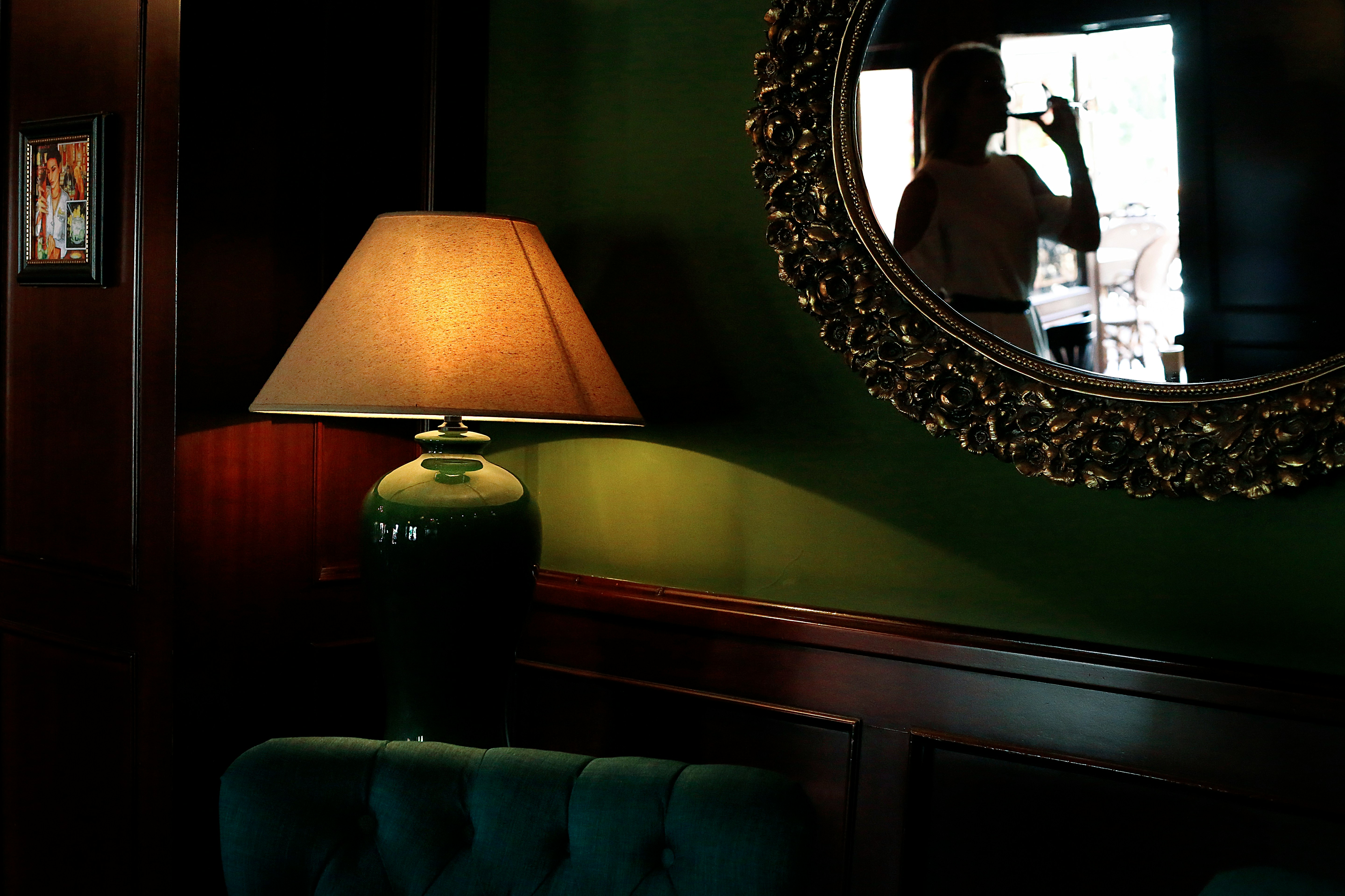 A traditional room with a lit lamp, reflecting a woman drinking from a glass.