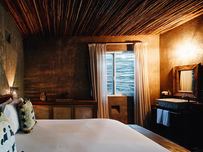 Jungle Room at Nômade Tulum with beautiful lamps, spacious bed, pillows, rug, sink, and mirror.