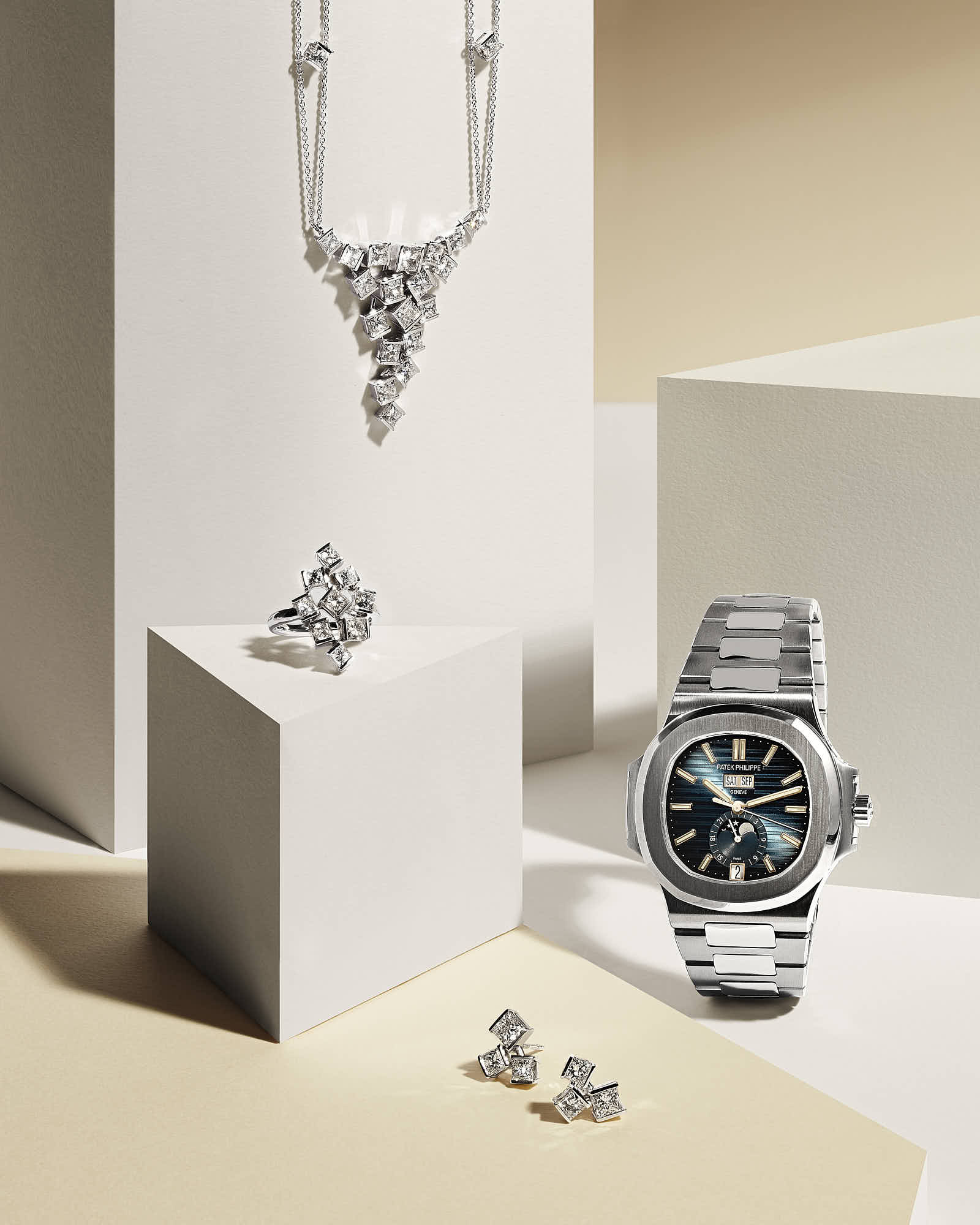 A sleek arrangement of silver jewelry: a necklace, earrings, and a watch displayed on minimalist pedestals.