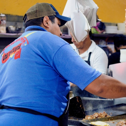 Sa isang masiglang taquería, isang taquero ang maingat na humihiwa ng adobo na baboy mula sa vertical na ihawan.