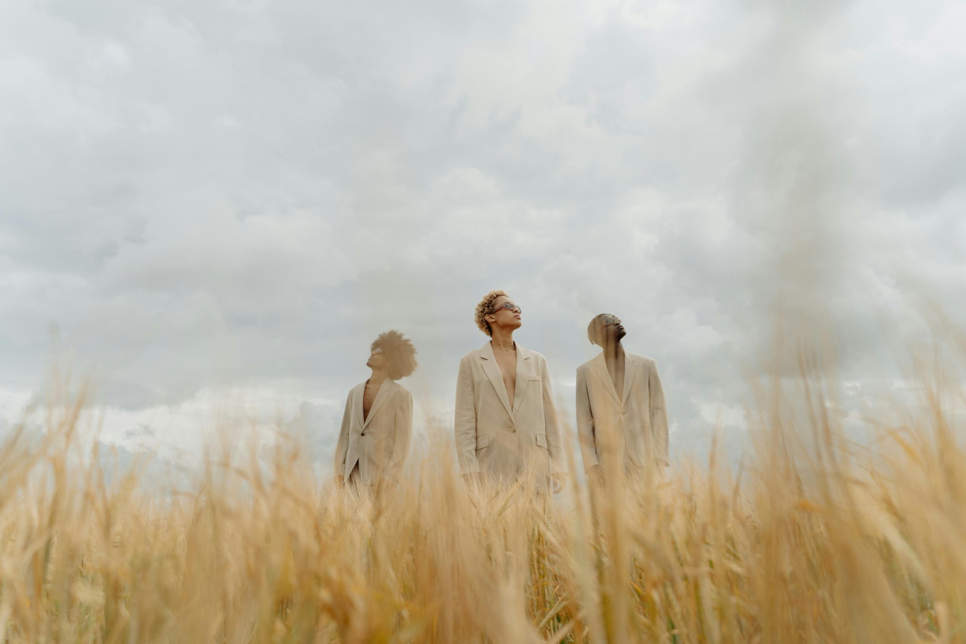 Three models standing in a wheat field, wearing beige suits.