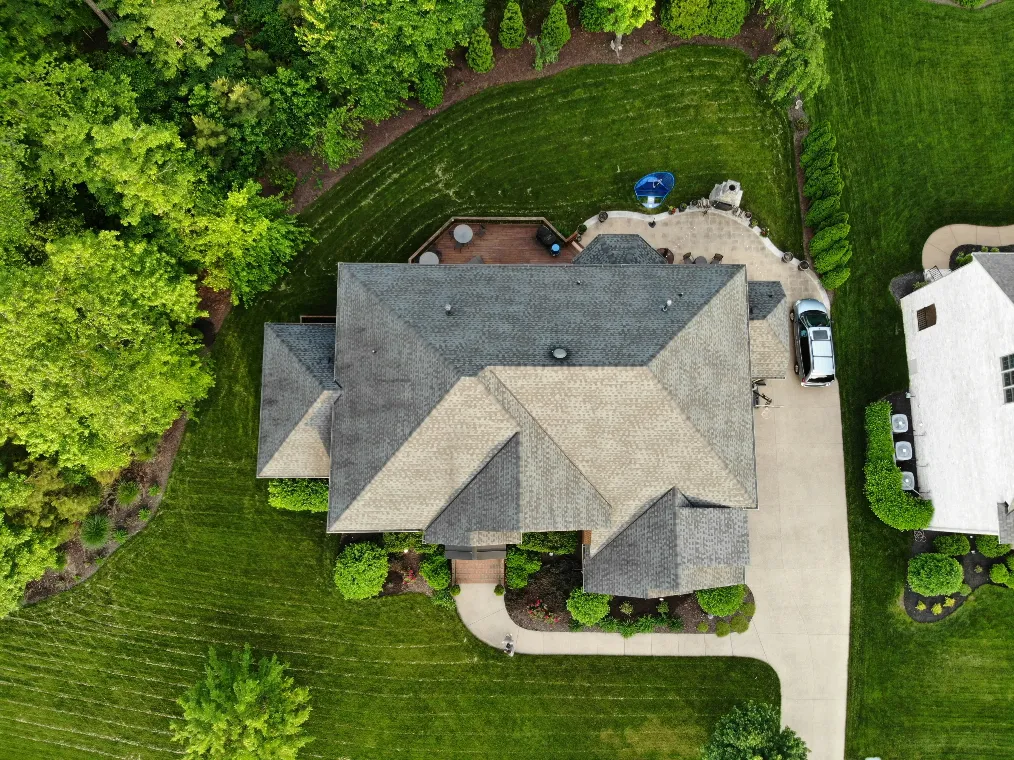 Top down aerial view of a well maintained home surrounded by trees with a curved driveway, landscaped yard, and backyard patio space. This real estate drone photography highlights the full property layout and natural surroundings, giving a drone videographer strong visuals to showcase privacy and outdoor living.