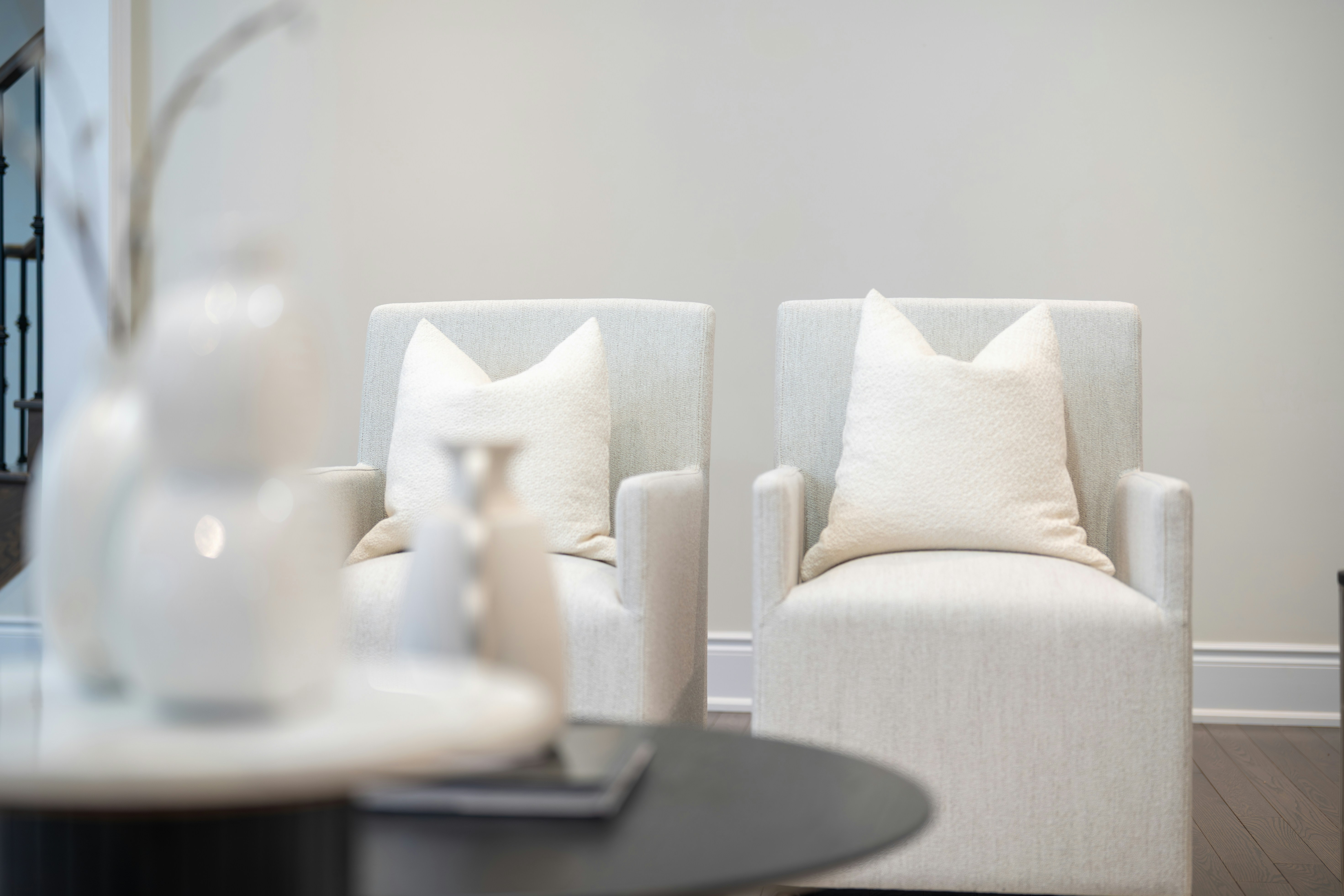 Two white armchairs with pillows in a room.