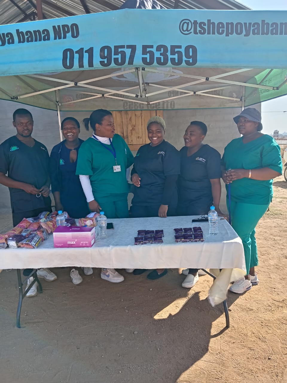 A smiling young man with crossed arms, wearing a plaid shirt and white t-shirt, poses against a dark background.