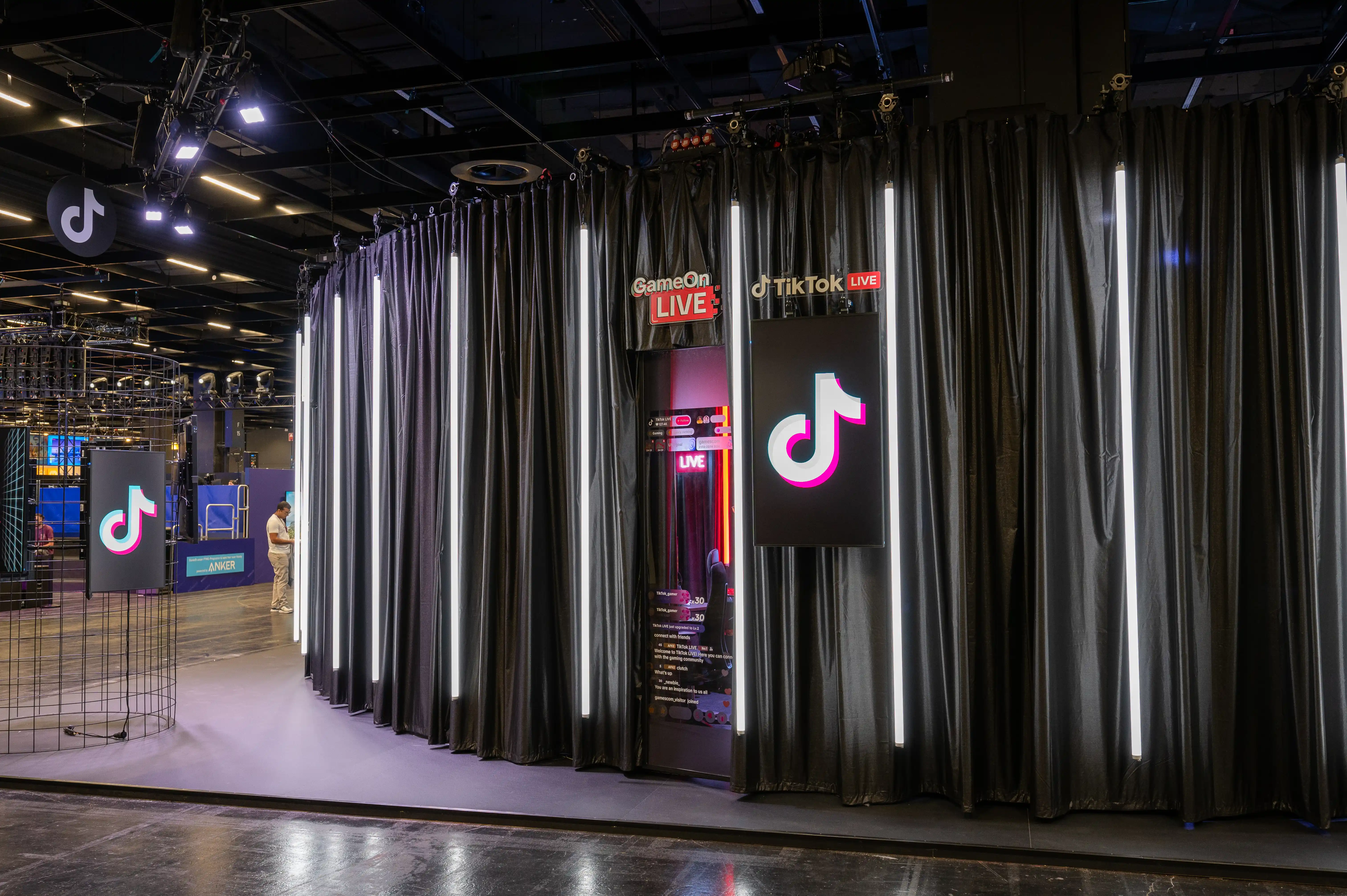 Curved black curtain facade with vertical light tubes and TikTok Live screens at the booth entrance at Gamescom.