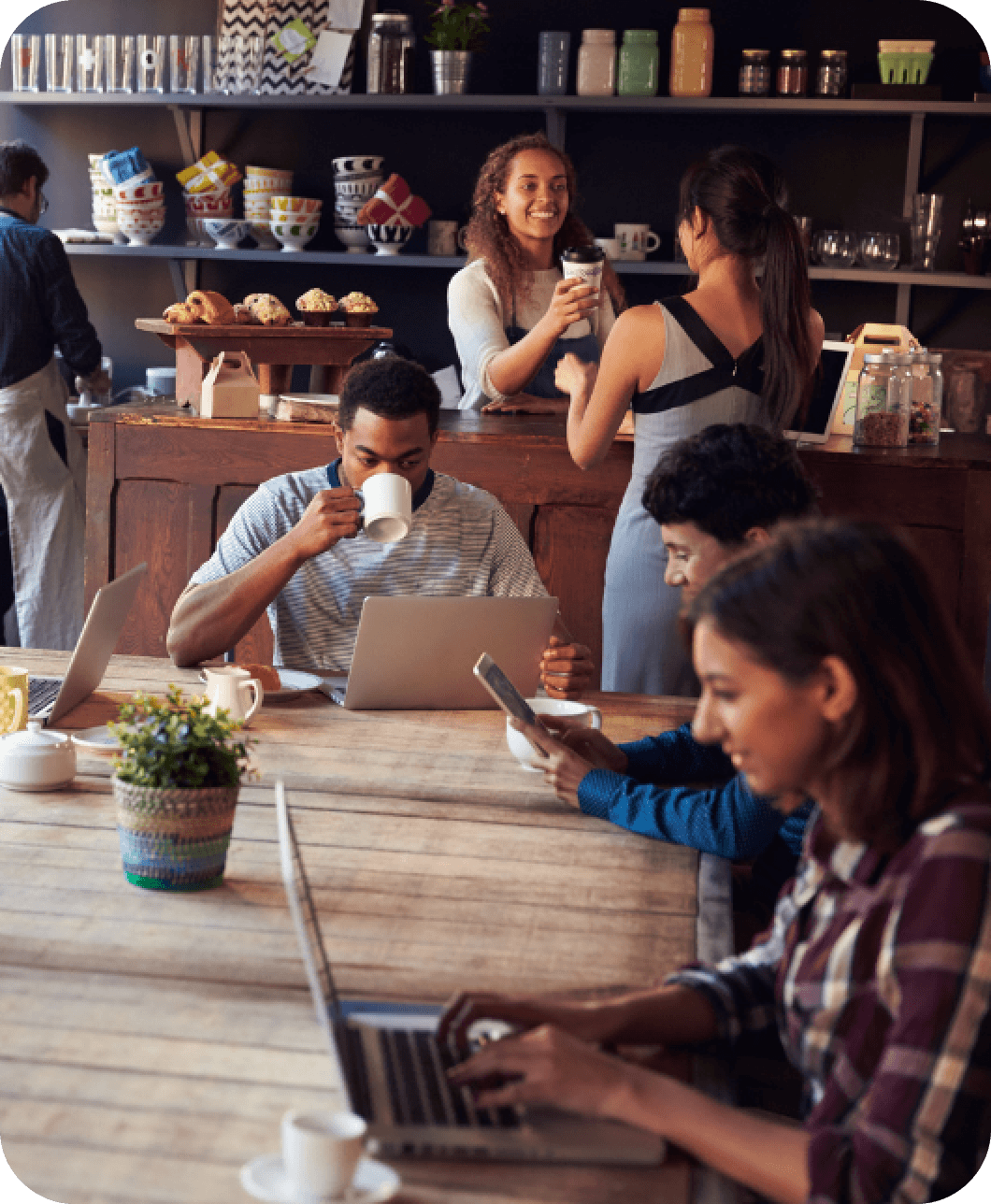 Busy coffee shop with customers using laptops and smartphones, connected to WiFipaysyou device providing high-speed Wi-Fi.