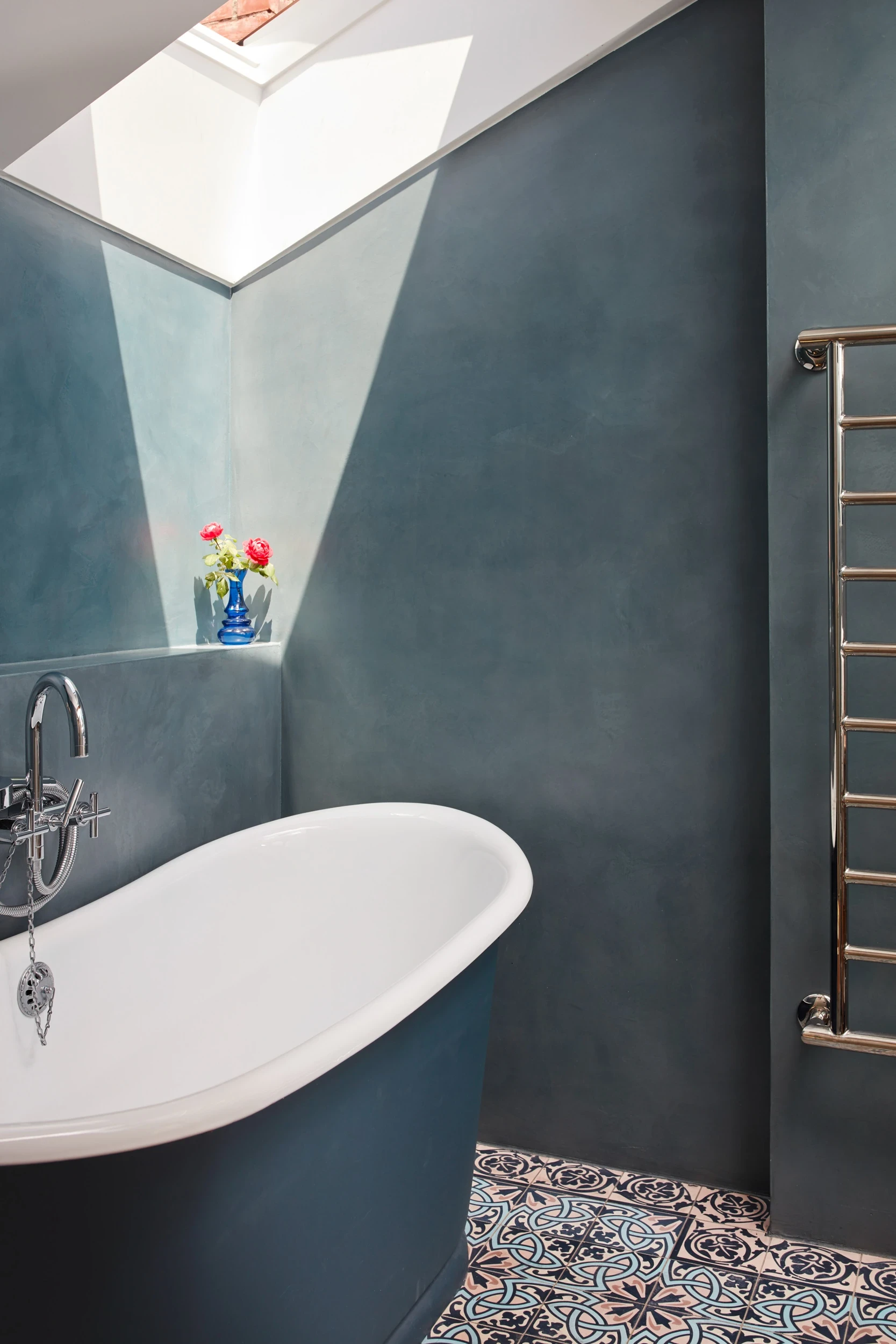 Salle de bain de la maison de village à Bugnaux, avec carreaux ciment, baignoire classique, murs en béton ciré bleu et oculus apportant une lumière naturelle remarquable.