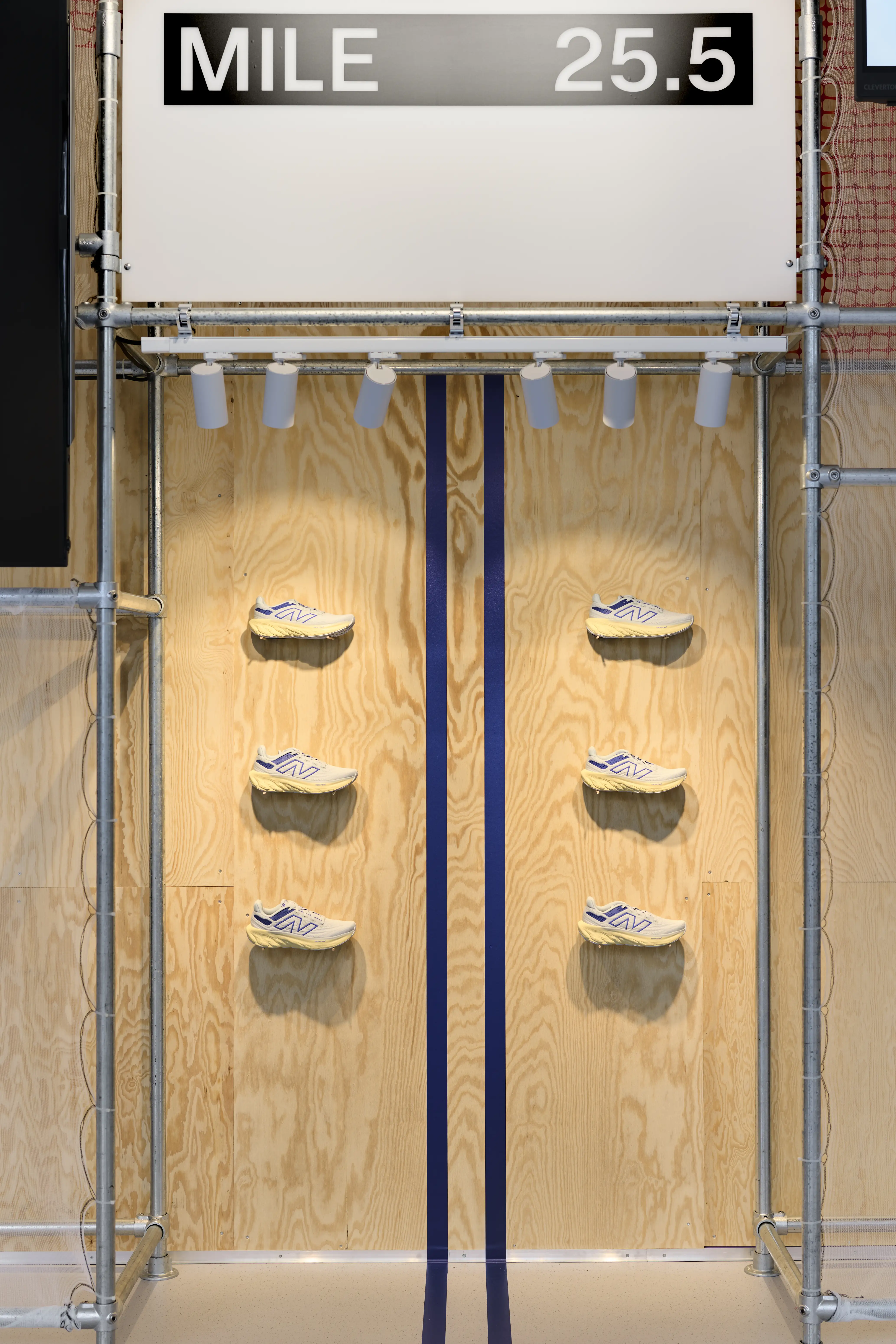 Plywood display wall with floating sneakers beneath a Mile 25.5 marathon sign at the Highsnobiety x New Balance pop-up.
