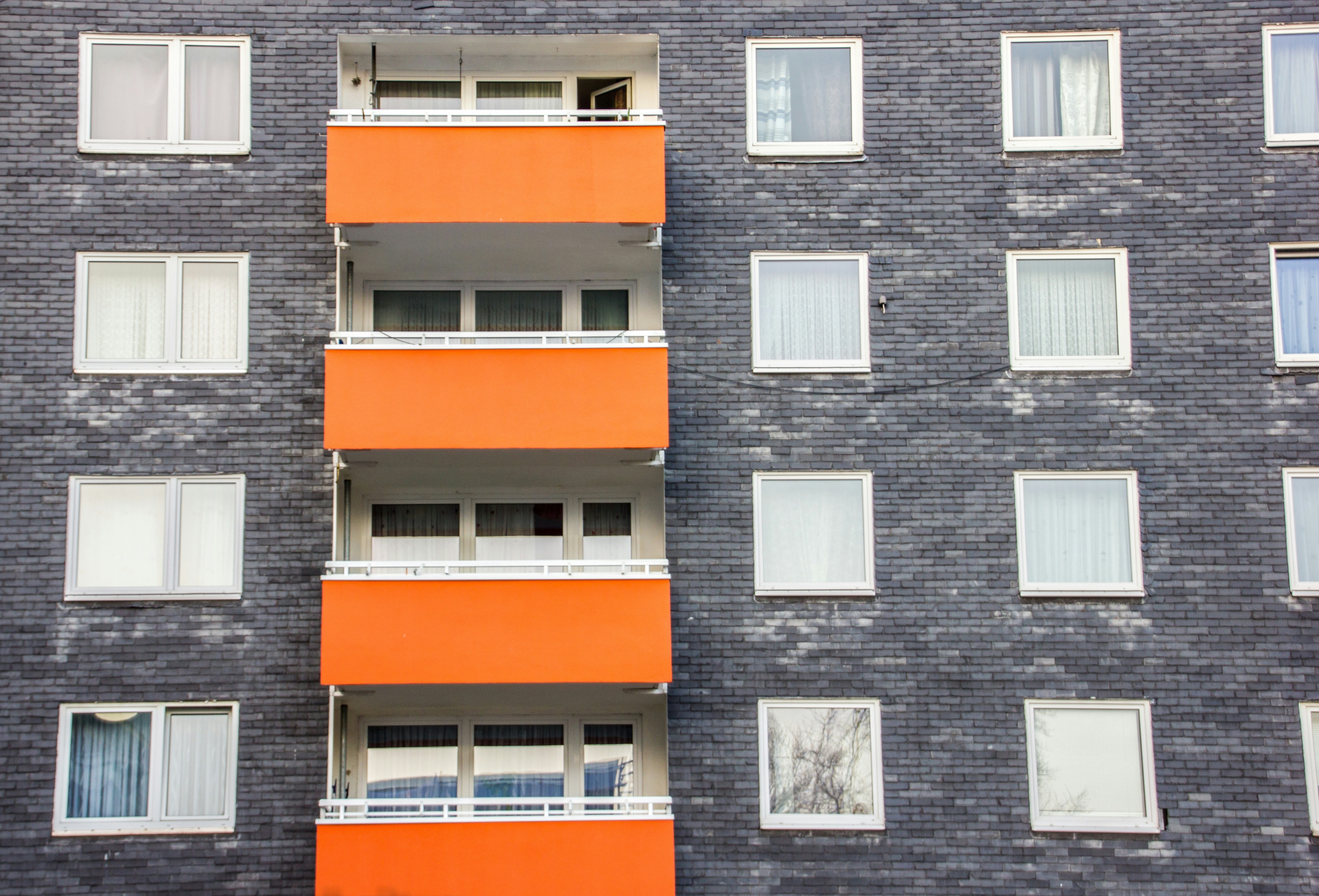 A grey apartment building with one column of orange balconies. 