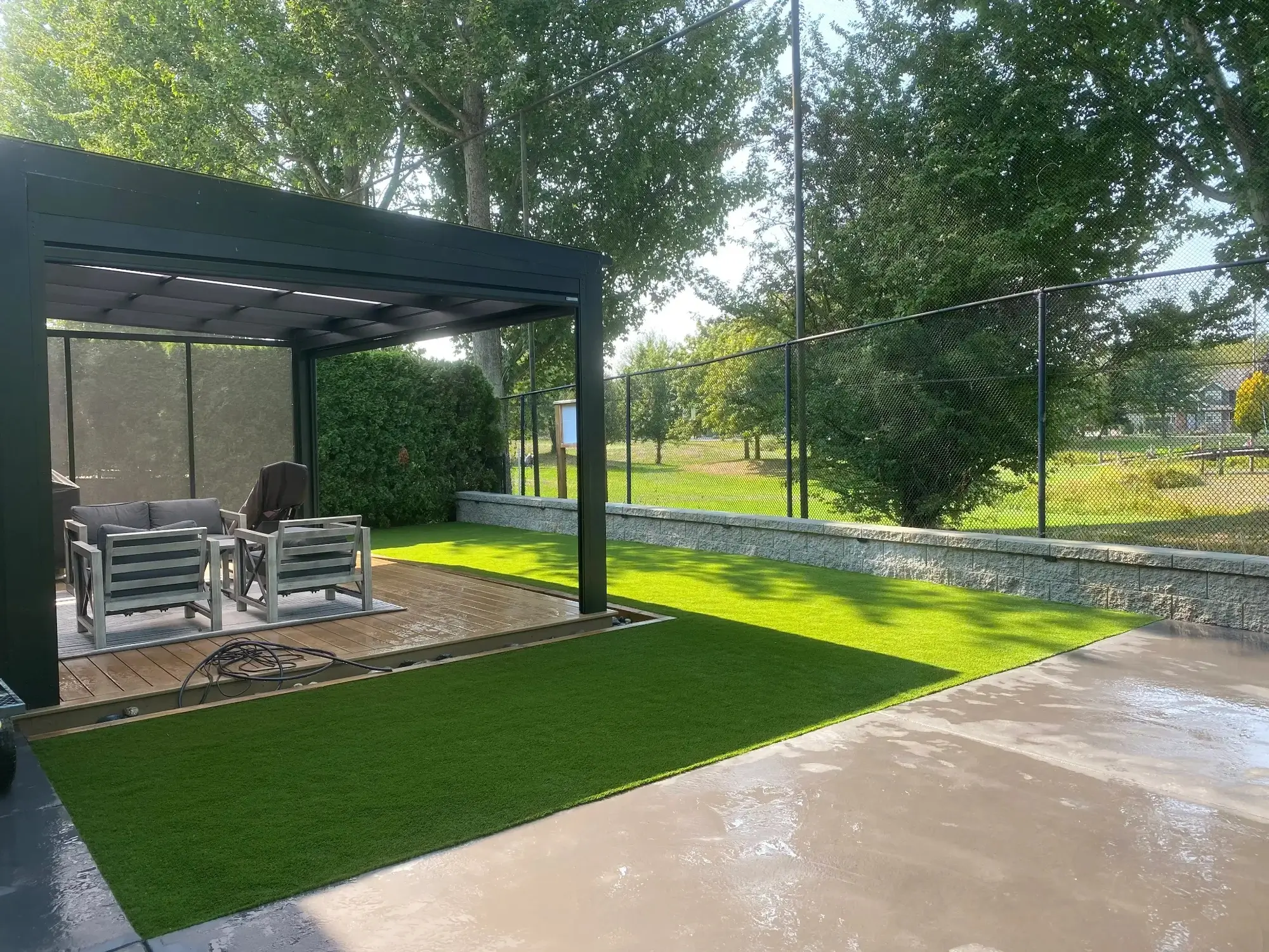 Landscaped backyard with artificial turf lawn, modern patio, and glass privacy fencing.