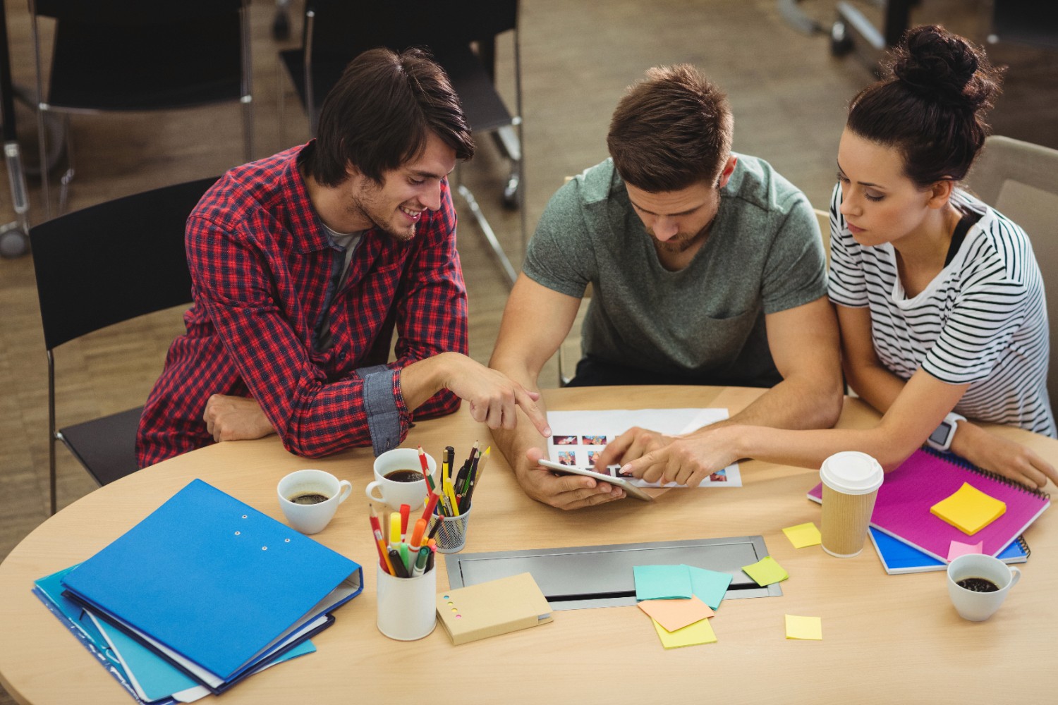 A group of three people gathered around a table, focused on a laptop, discussing ideas and sharing insights.