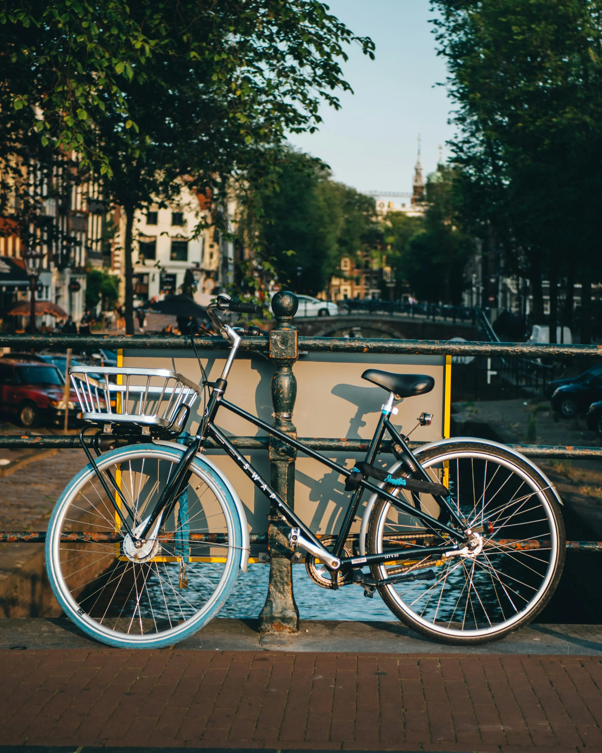 Black bicycle with a basket parked next to a canal in Amsterdam.