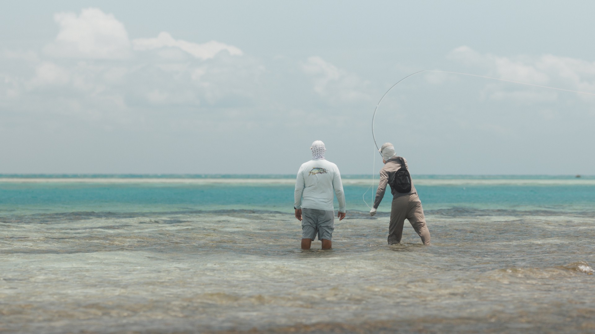 Guide Marlon Leslie standing side by side a saltwater angler that's casting a fly fishing rod on a knee deep flat
