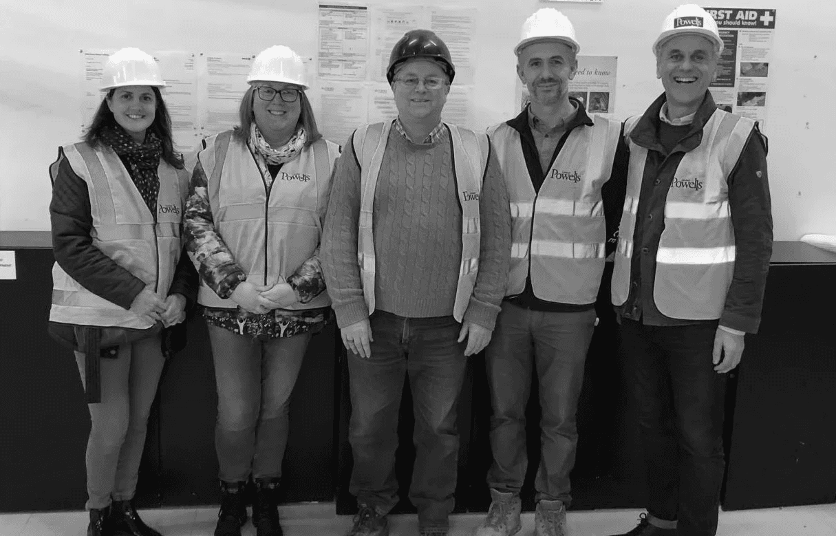 Black and white image of people working at a table with laptops, showing hands gesturing during discussion of digital content displayed on screens, with fabrica® logo in the corner.