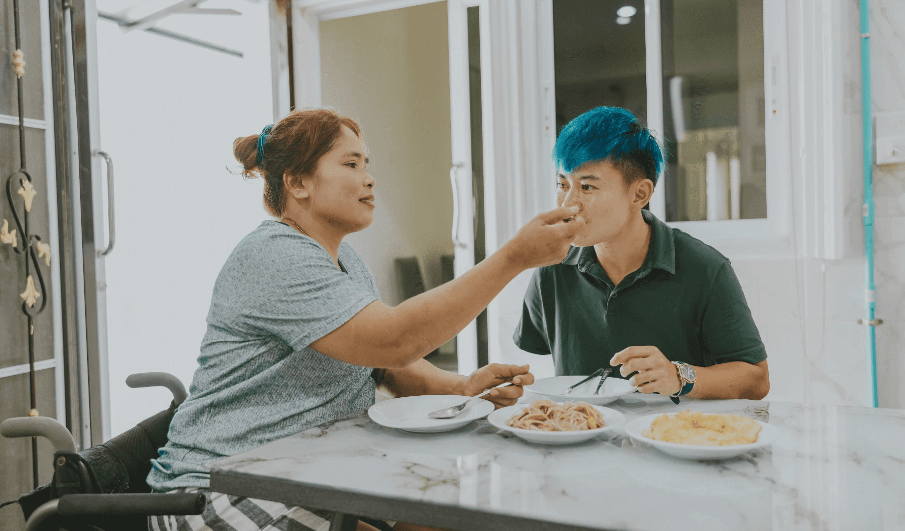 Two people sharing a meal at a table, with one feeding the other playfully in a casual setting.