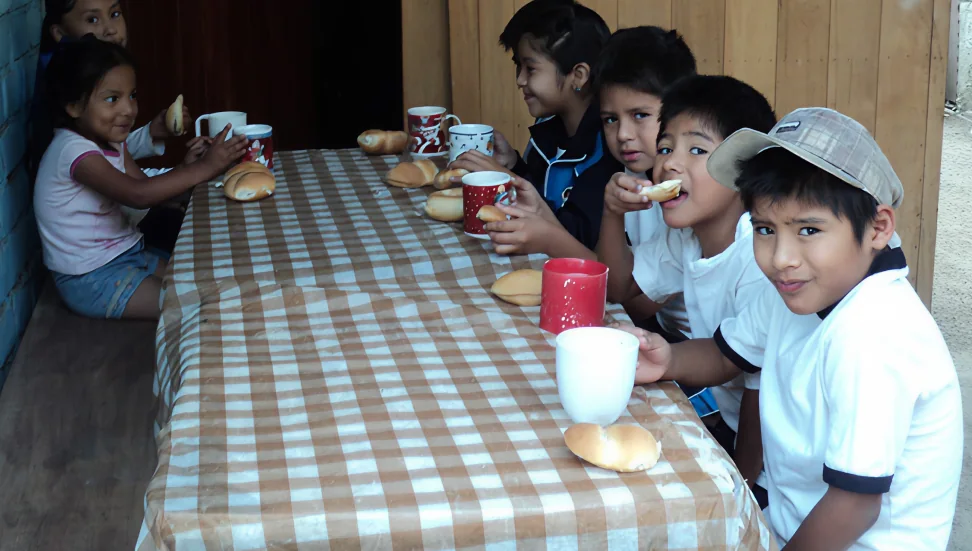 Grupo de niños sonriendo mientras desayunan juntos en una mesa con mantel de cuadros.