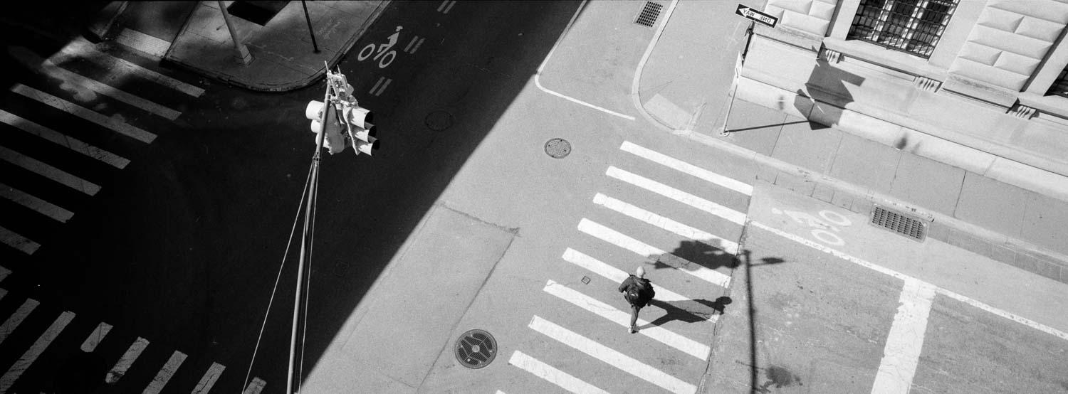 Fujifilm TX-1 panoramic photo of a top view of a person walking down the street in Manhattan in New York City, with strong afternoon light and strong use of geometry.