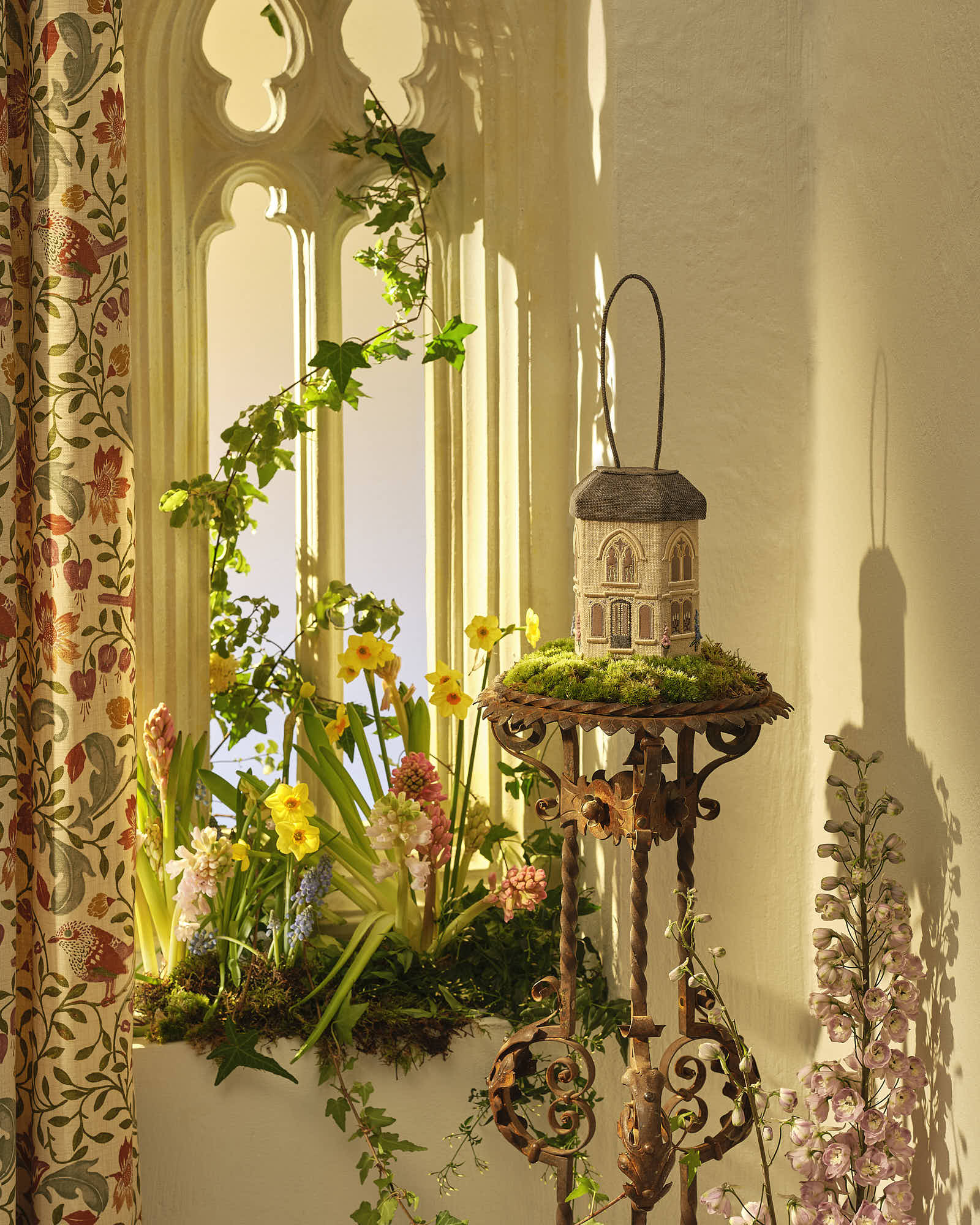 Vintage garden-themed window display with flowers and ornate stand.
