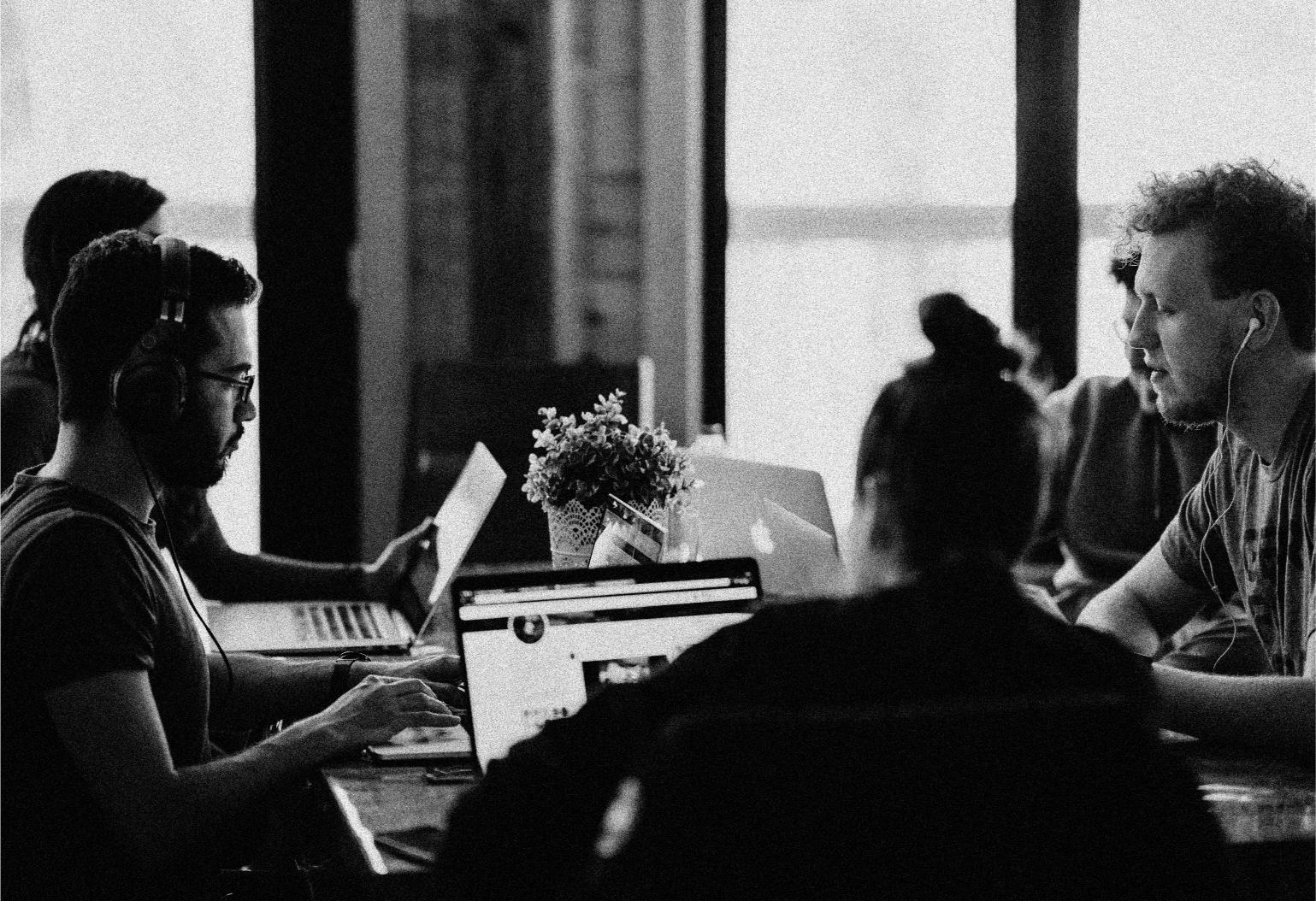 Backside of a person with a had and curly hairs sits in front of a screen in a room