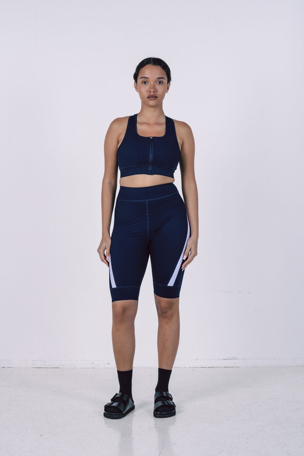 Woman-wearing-a-navy-blue-cycling-set-featuring-a-zip-up-front- sports-bra-and-matching-high-rise- biker-shorts-with-white-angled-stripe-detail-Perfect-for-workouts