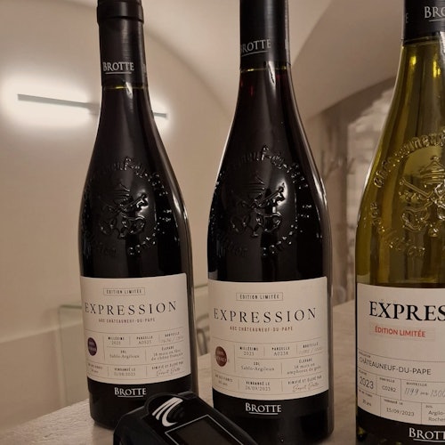 Tri boce vina Brotte s oznakom „Expression”, jedna žuta i dvije tamne, postavljene na stol uz digitalni uređaj.