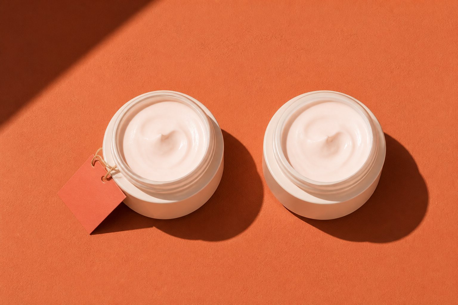 Two nearly identical cream jars side by side, one with a small coral tag and one without