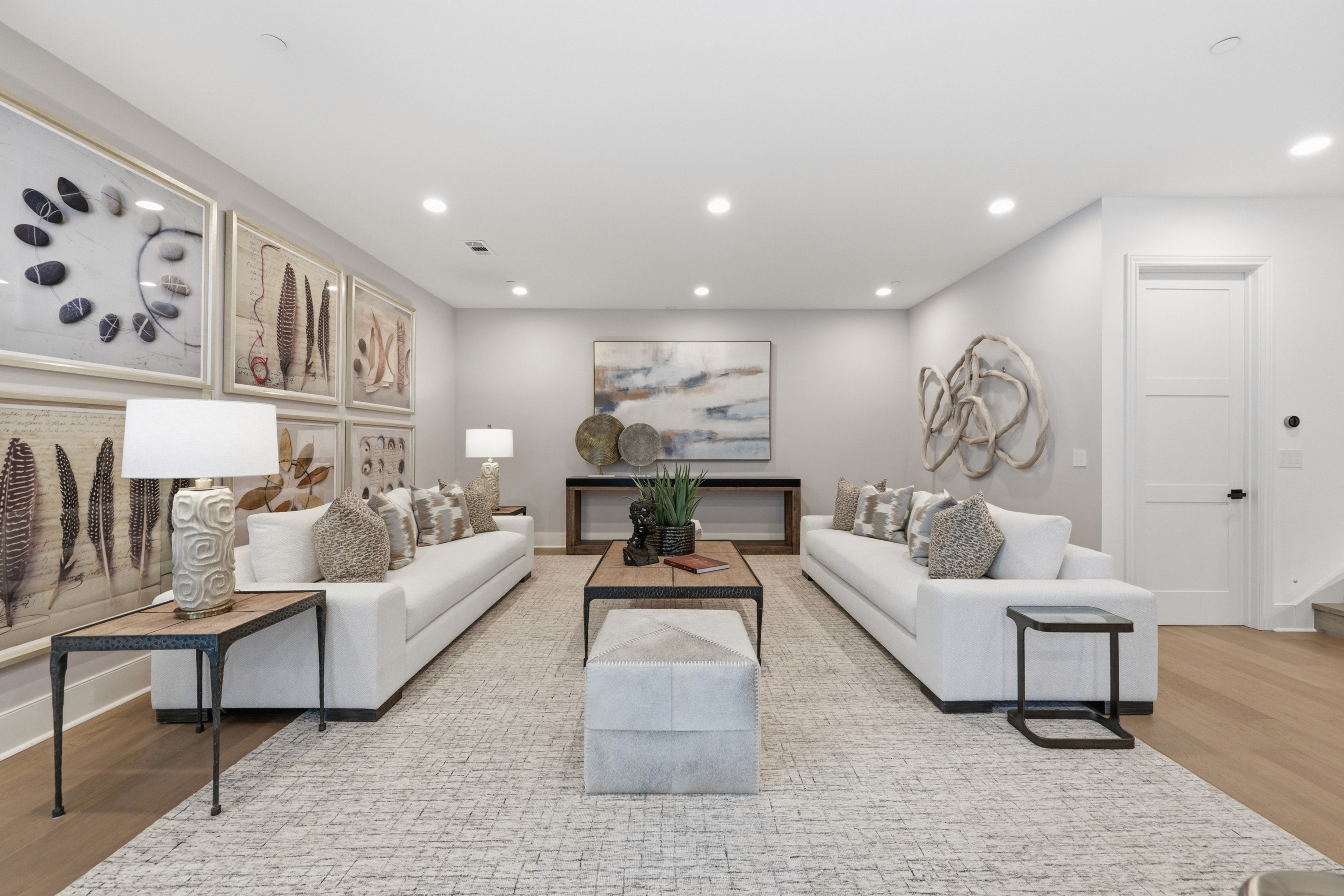 Lower-level lounge with white sofas, an ottoman, and a gallery wall of framed art.