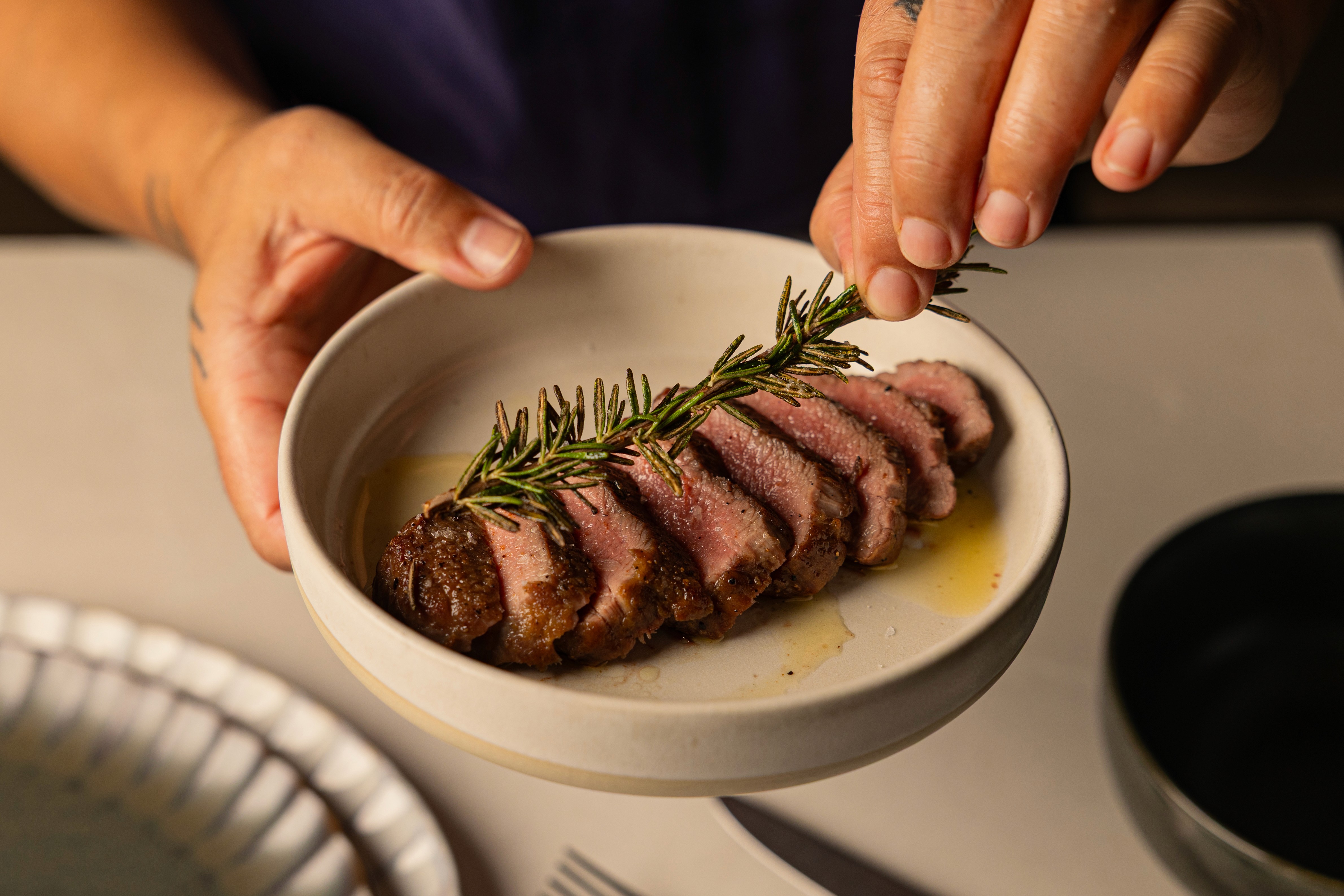 Chef holding a plate of lightly oiled sliced beef filet, with a rosemary twig in hand