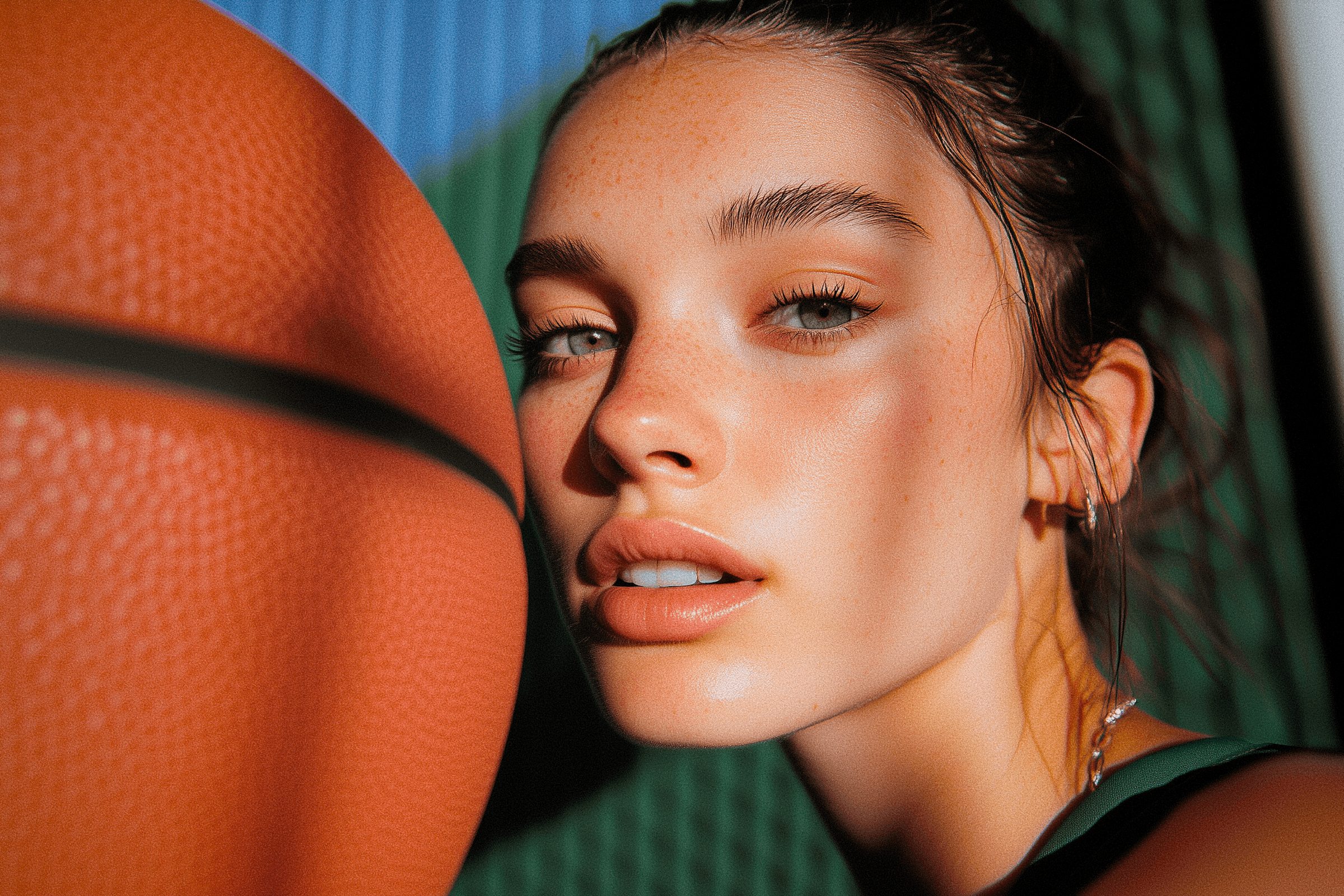 Close-up of a young woman with green eyes and freckles, holding a basketball. Intense gaze and soft lighting create a striking portrait.