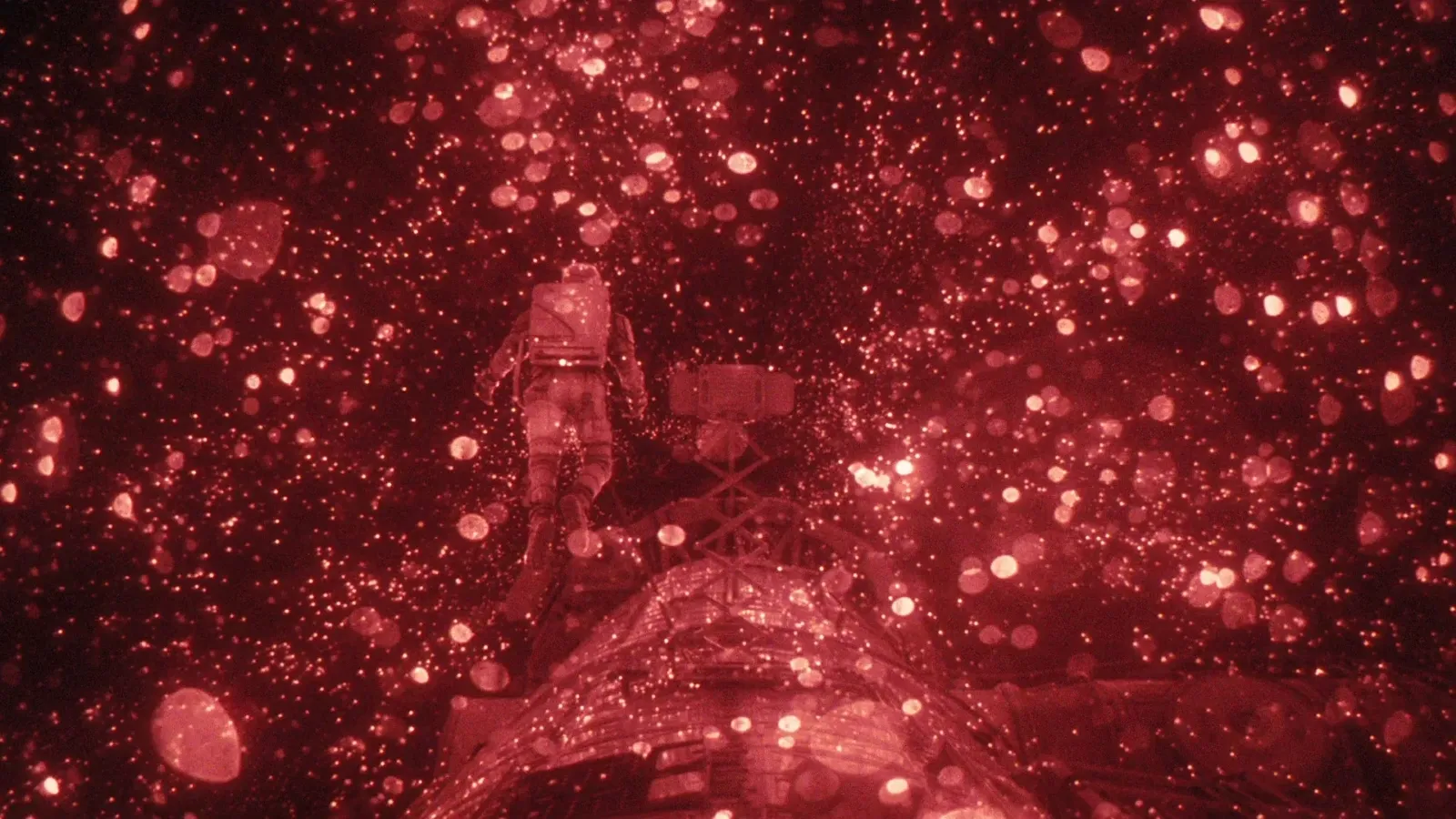 A lone astronaut, illuminated by a reddish glow, floats amidst a mesmerizing flurry of sparkling particles in space, creating an ethereal and otherworldly atmosphere.