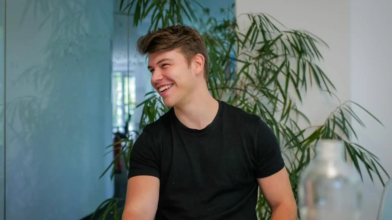 Samuel Mitterrutzner, CTO of CoachingArea, sits in a modern office and smiles. Plants can be seen in the background, creating a relaxed atmosphere. The picture shows him during an interview in which he talks about his career from footballer to software development.