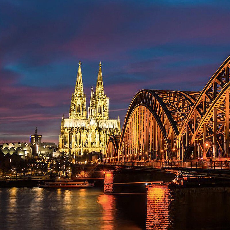 New York City skyline at twilight featuring the Empire State Building and other skyscrapers illuminated against a purple-blue sky.